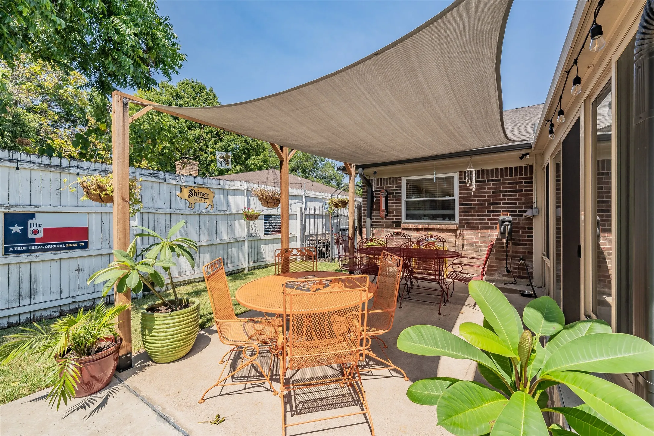 Expansive concrete patio featuring a shade sail, brick exterior, string lighting, and direct exterior access