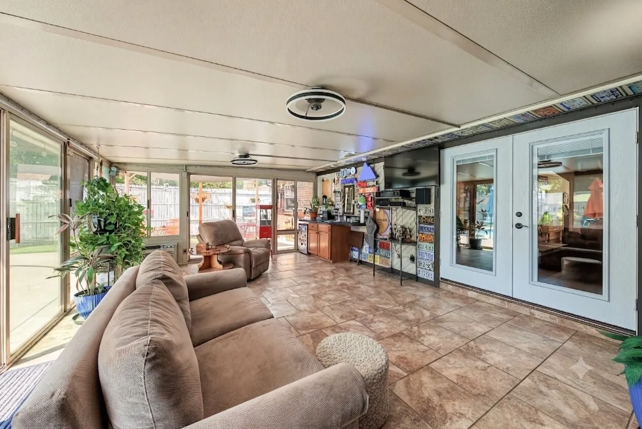 Enclosed sun room with tile flooring, 2 sliding glass doors, dual ceiling light fixtures, and white French patio doors