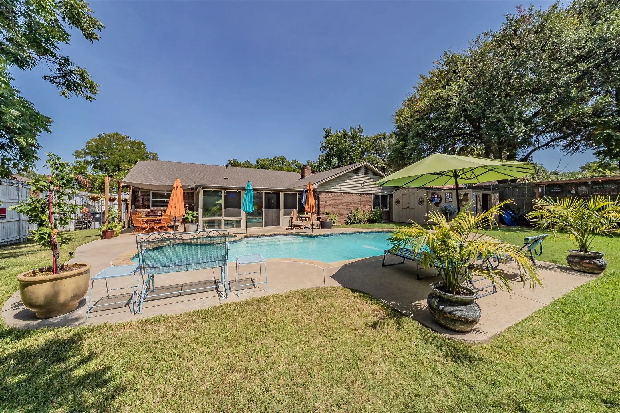Outdoor swimming pool with concrete surround, expansive grass lawn, and a rear patio with a covered section mature landscaping and flower gardens