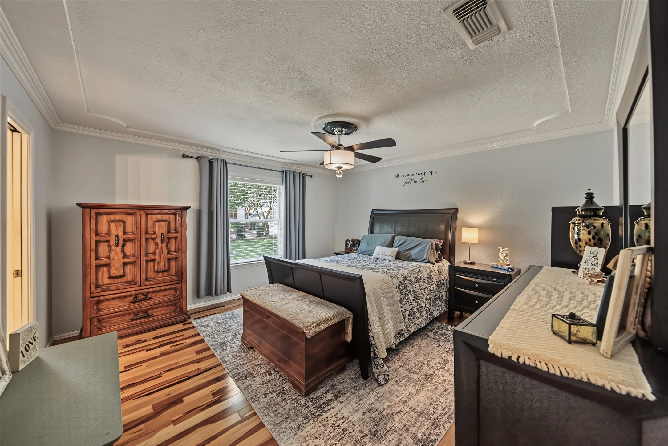 Tray ceiling with crown molding, wood-finish flooring, ceiling fan with integrated lighting, and a window with natural light