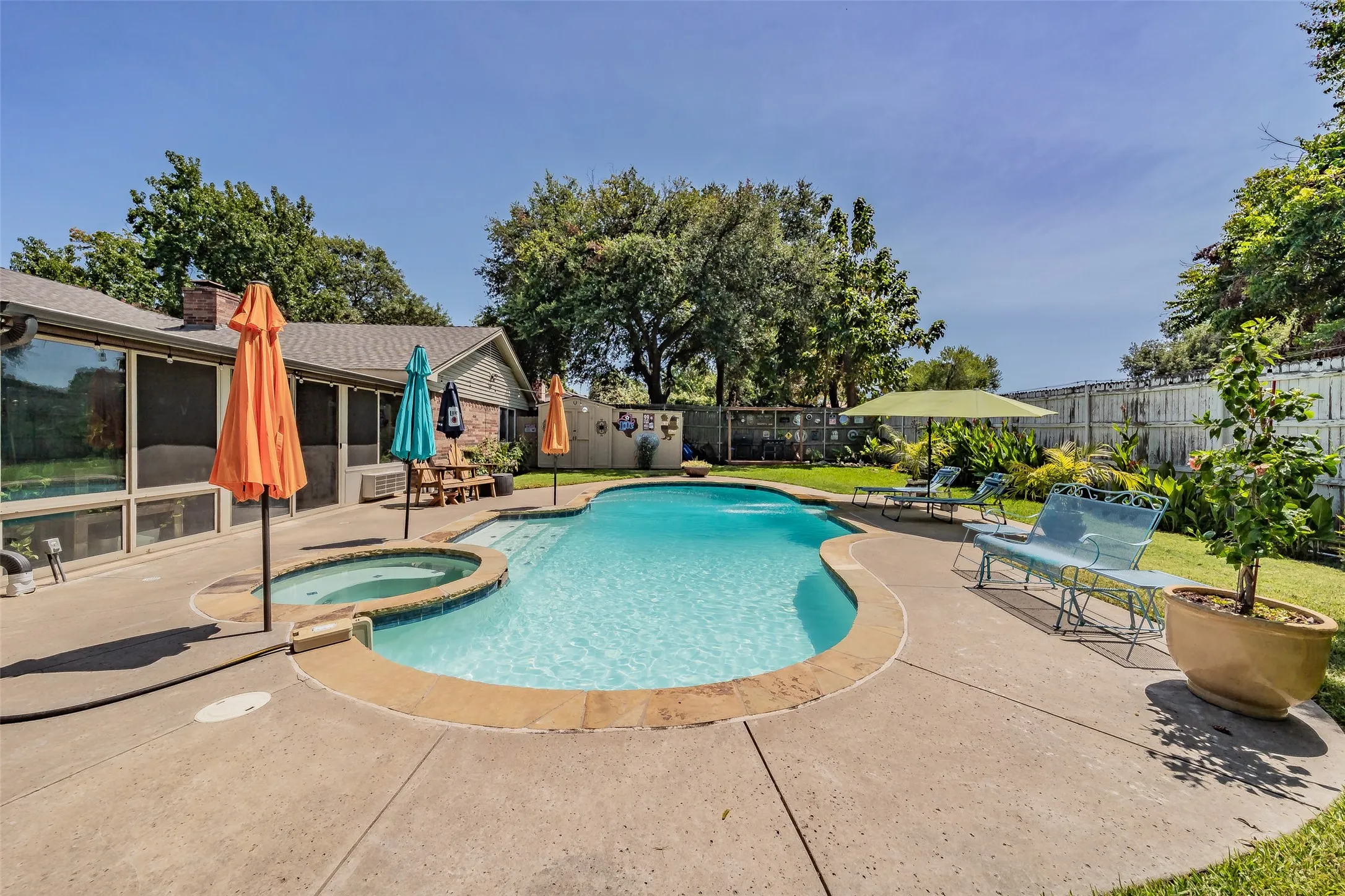 Curved in-ground swimming pool with an integrated hot tub, surrounded by a concrete patio for seating and relaxation