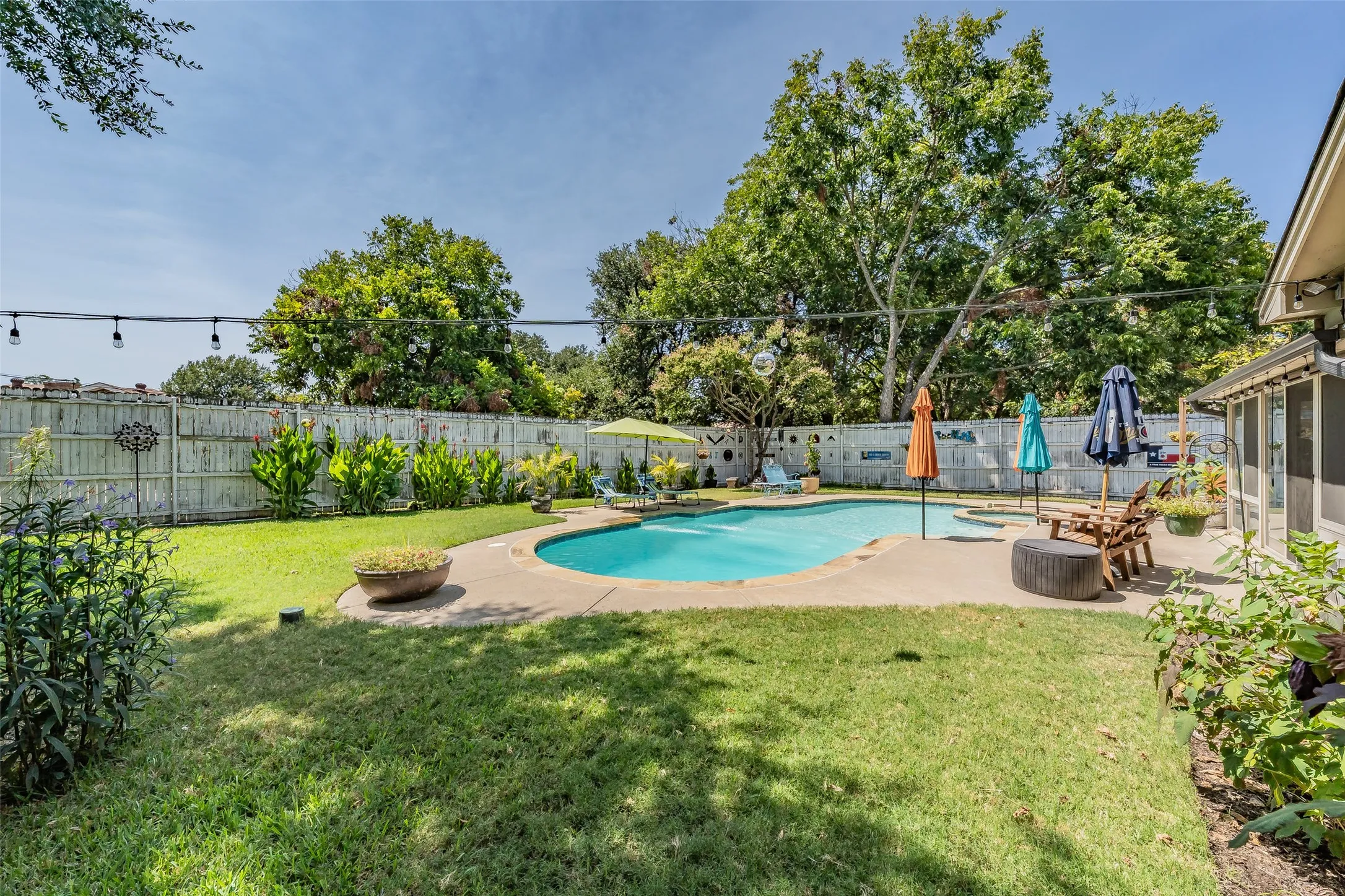 Private backyard with a freeform swimming pool, surrounding concrete patio, and mature perimeter trees and 8ft wood privacy fence