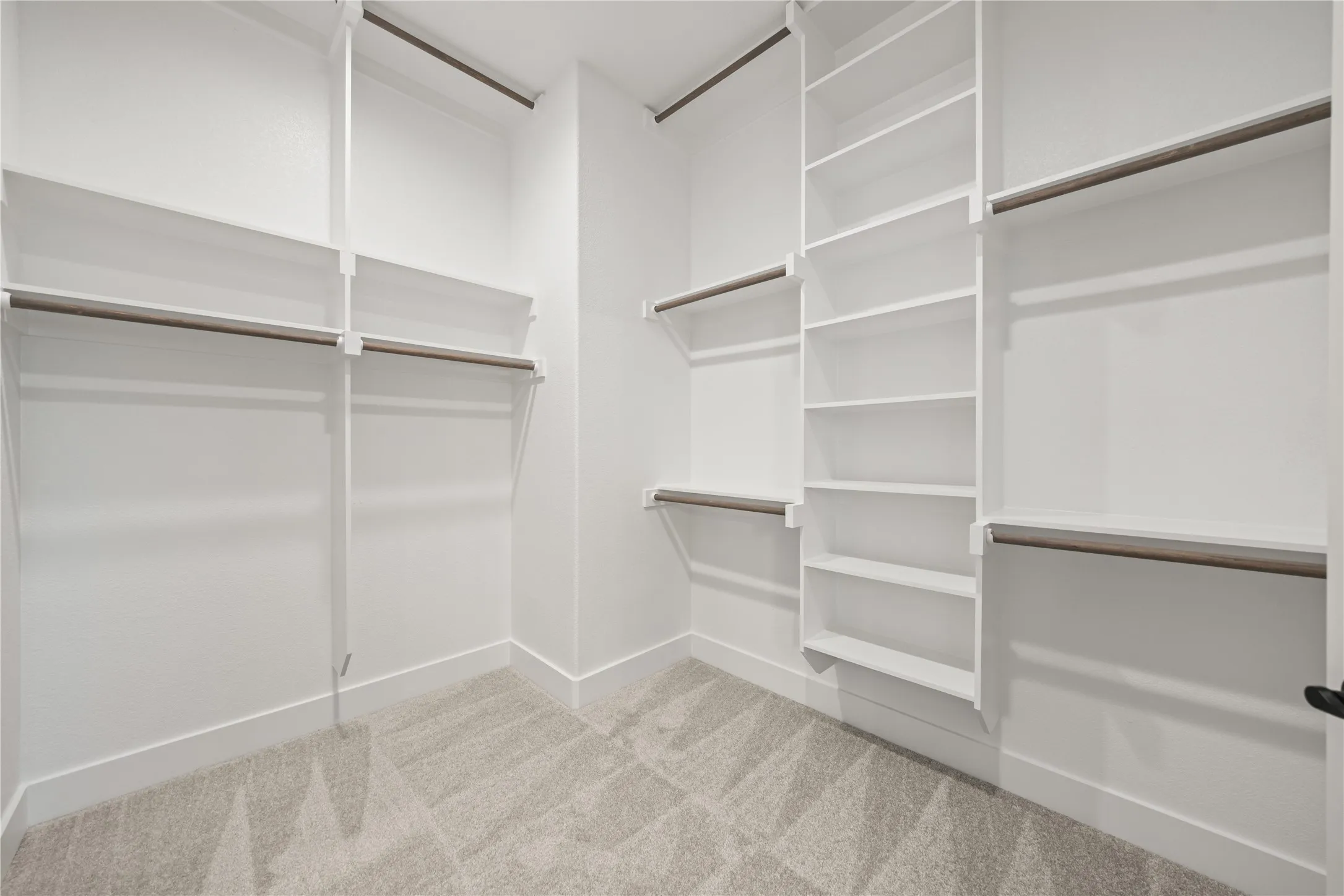 Walk-in closet featuring white built-in shelving, multiple hanging rods, and neutral-toned carpeting