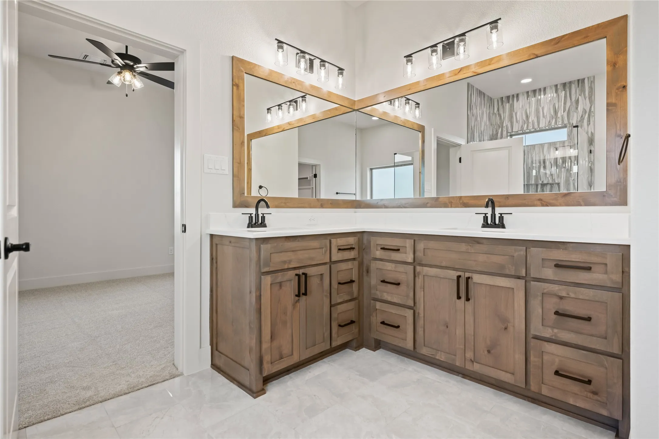 Dual wood-frame mirrors above a corner vanity with wood-finish cabinetry, white countertops, and matte black fixtures