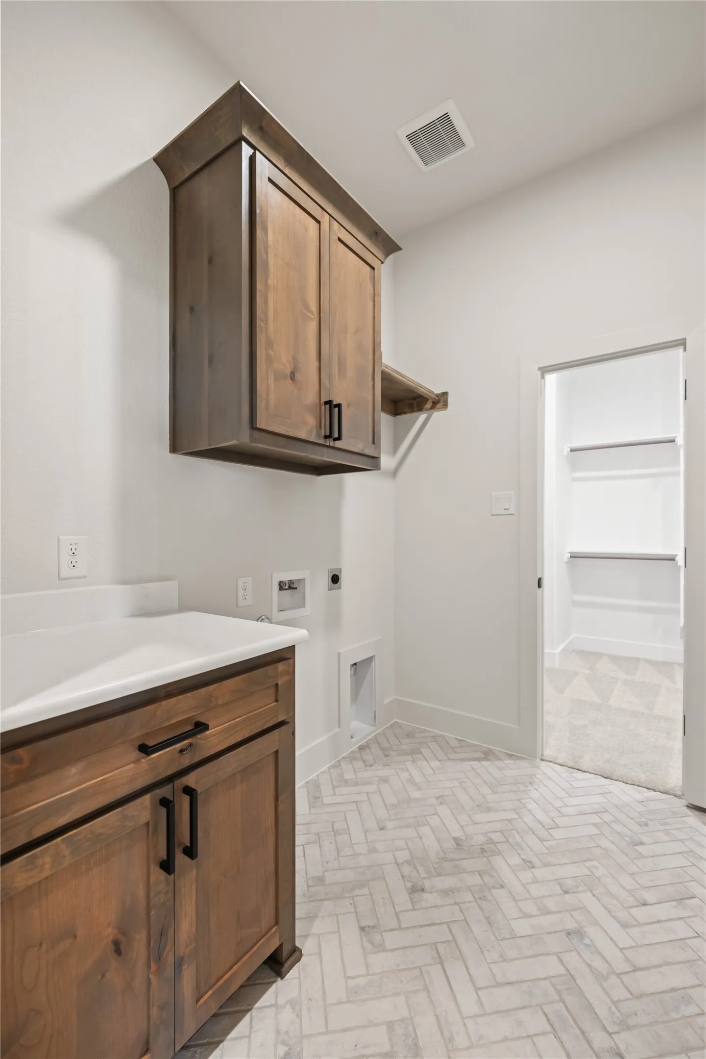 Herringbone-patterned flooring, wood-finish cabinetry, quartz-finish countertop, and ample built-in storage