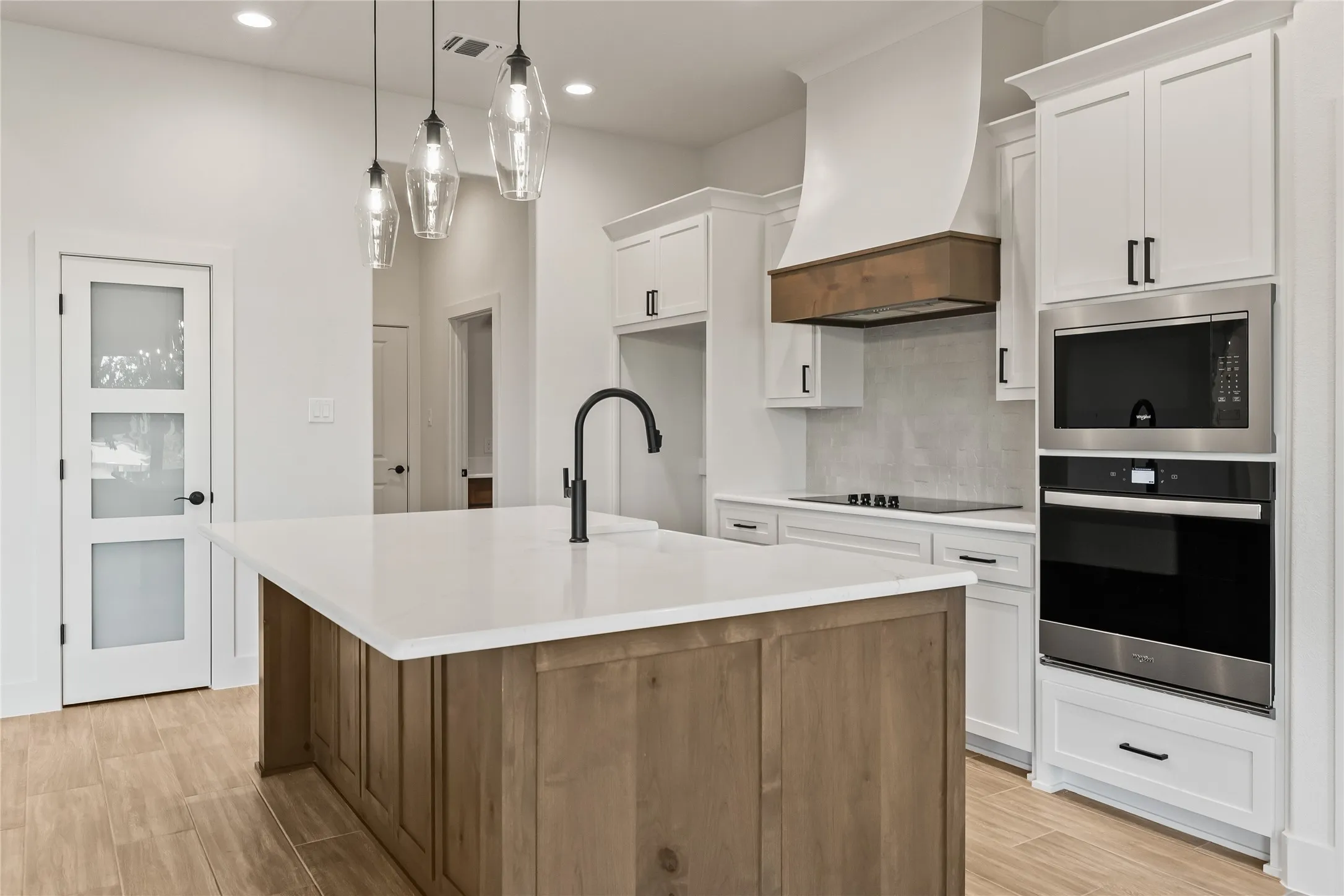 Kitchen featuring a center island with a white countertop, white cabinetry, integrated stainless steel appliances, a wood-finish range hood, and wood-finish flooring
