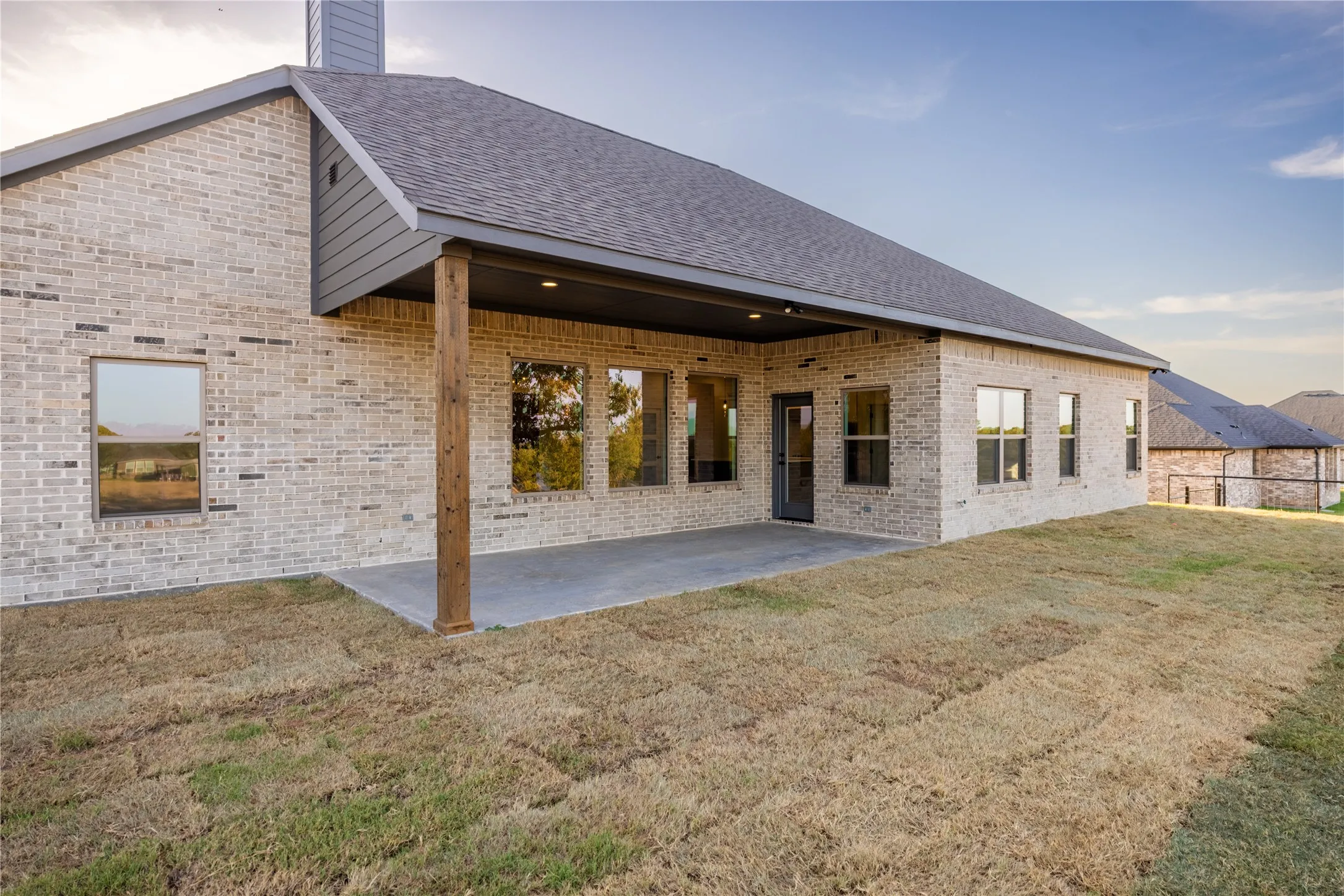 Expansive backyard featuring a covered patio with a wood-finish support beam, light brick exterior, and multiple windows