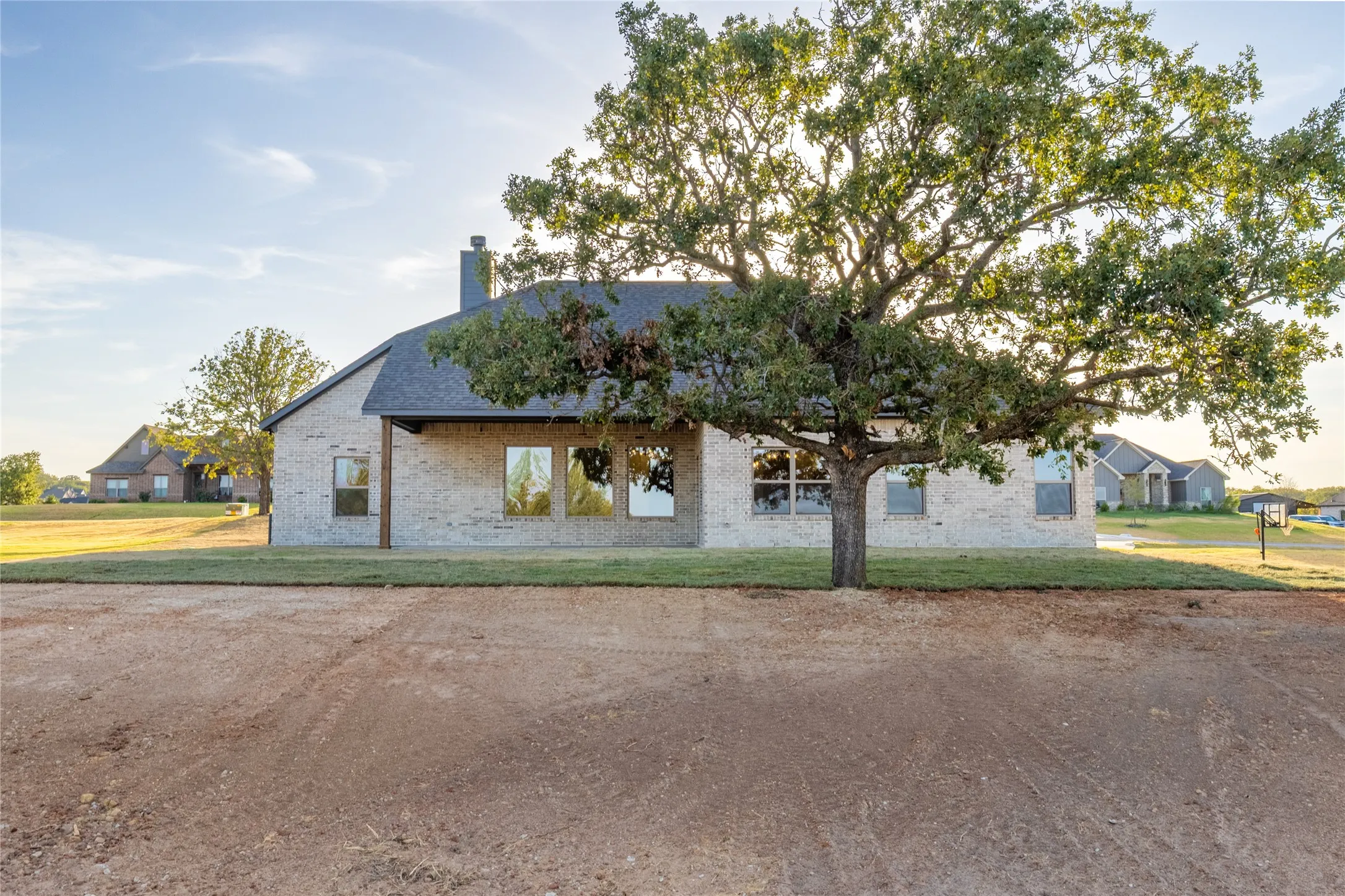 Brick exterior with dark roof and chimney, featuring multiple windows and a covered entry, set against a backdrop of mature trees and established landscaping