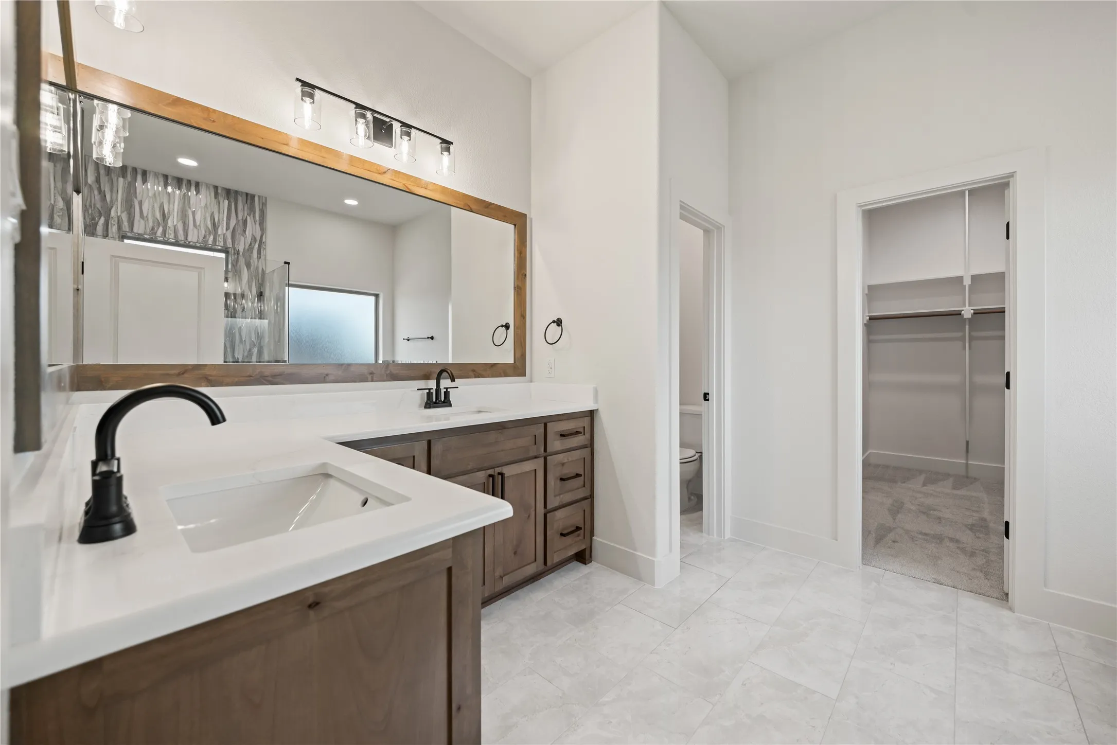 Dual vanity with wood-finish cabinetry, white countertops, and matte black fixtures