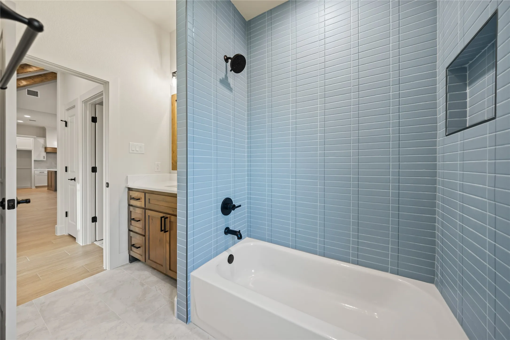 Bathroom featuring a built-in bathtub, light blue subway tile surround, recessed shower niche, wood-finish vanity with countertop, and black fixtures