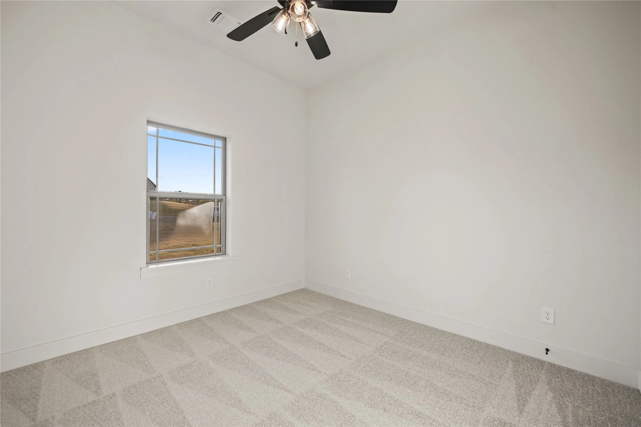 Neutral wall paint, ceiling fan with integrated lighting, window with a white frame, light-toned patterned carpet, and recessed ceiling vent