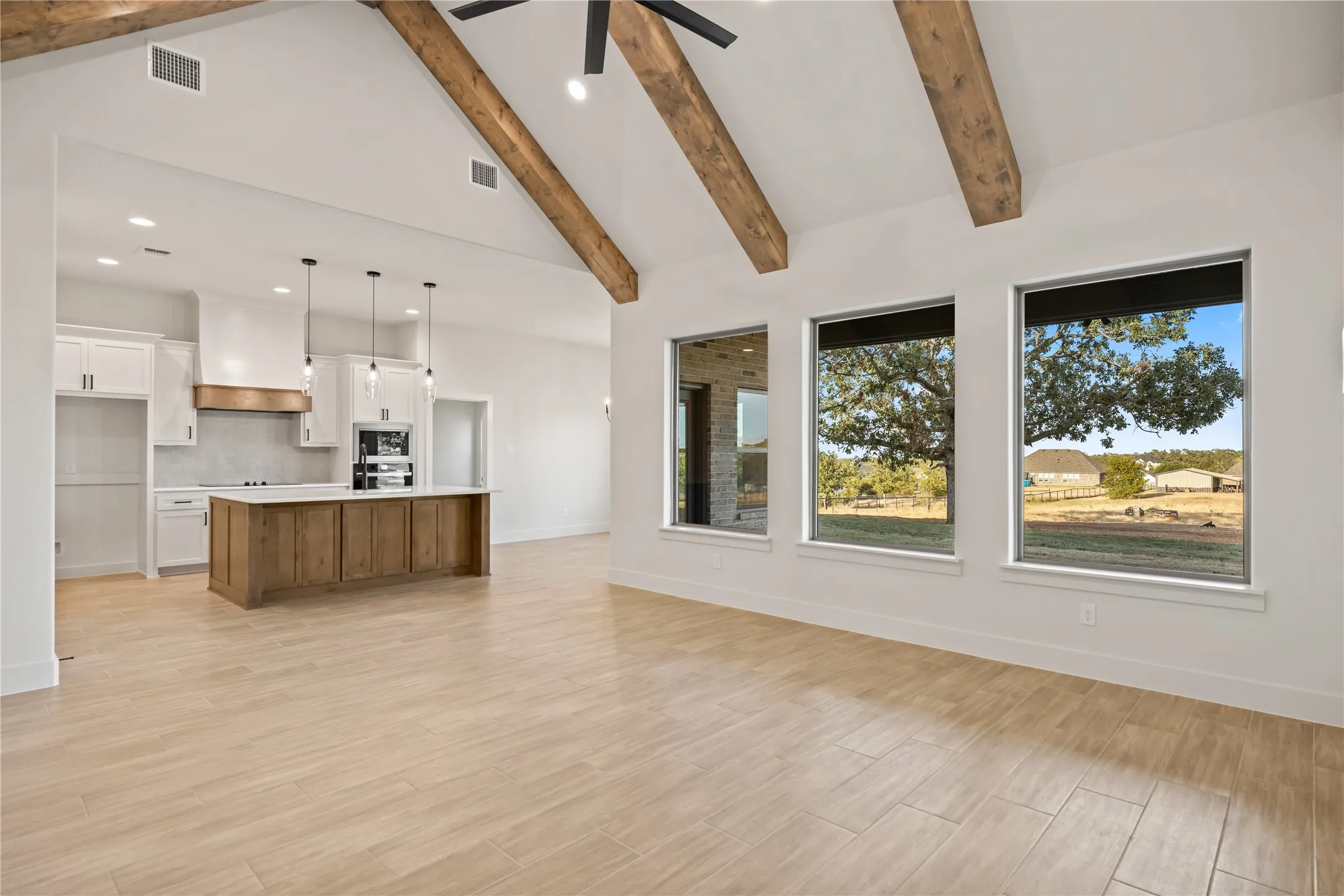 Vaulted ceiling with exposed wood beams, wood-finish flooring, white kitchen cabinetry, wood-paneled kitchen island, and multiple windows