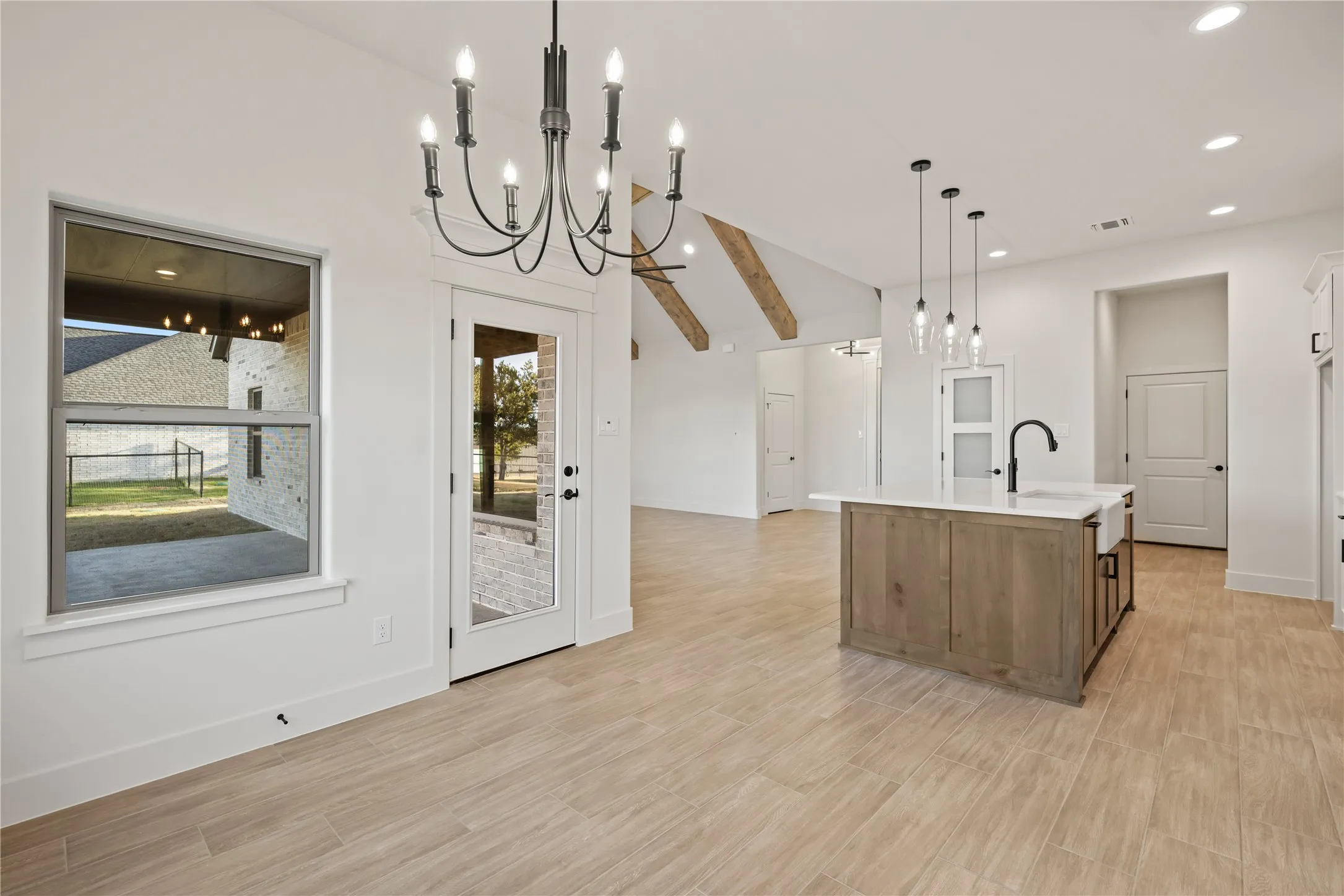 Open-concept space featuring wood-finish flooring, a kitchen island with a farmhouse sink, and vaulted ceilings with exposed beams