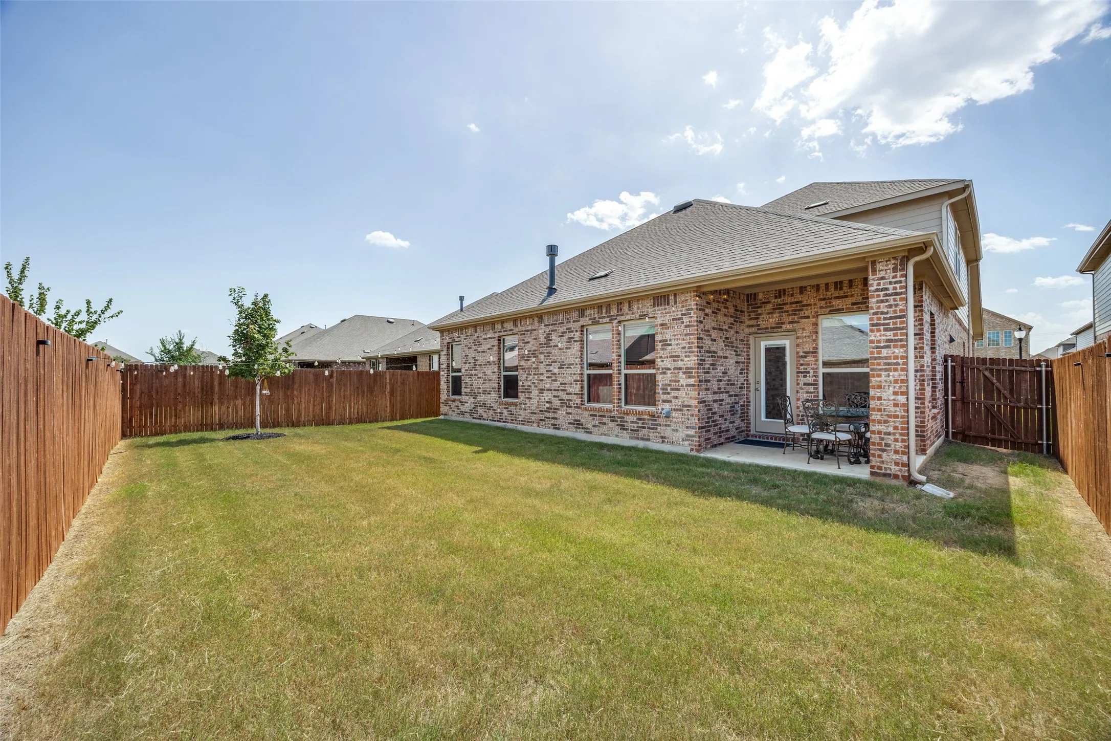 Fenced backyard featuring a manicured lawn, brick exterior, and covered patio