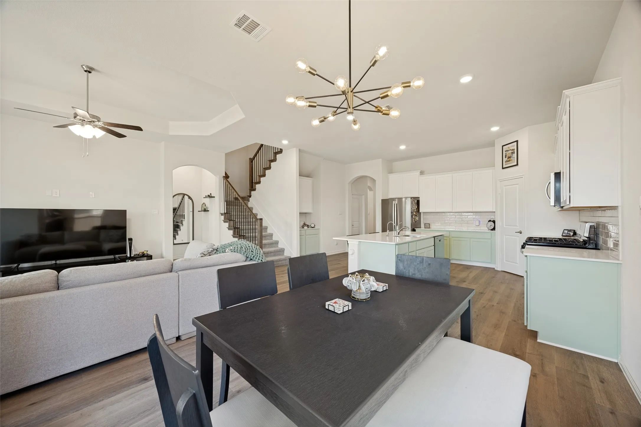 Open concept living space featuring wood-finish flooring, a kitchen island with seating, recessed lighting, and a modern chandelier