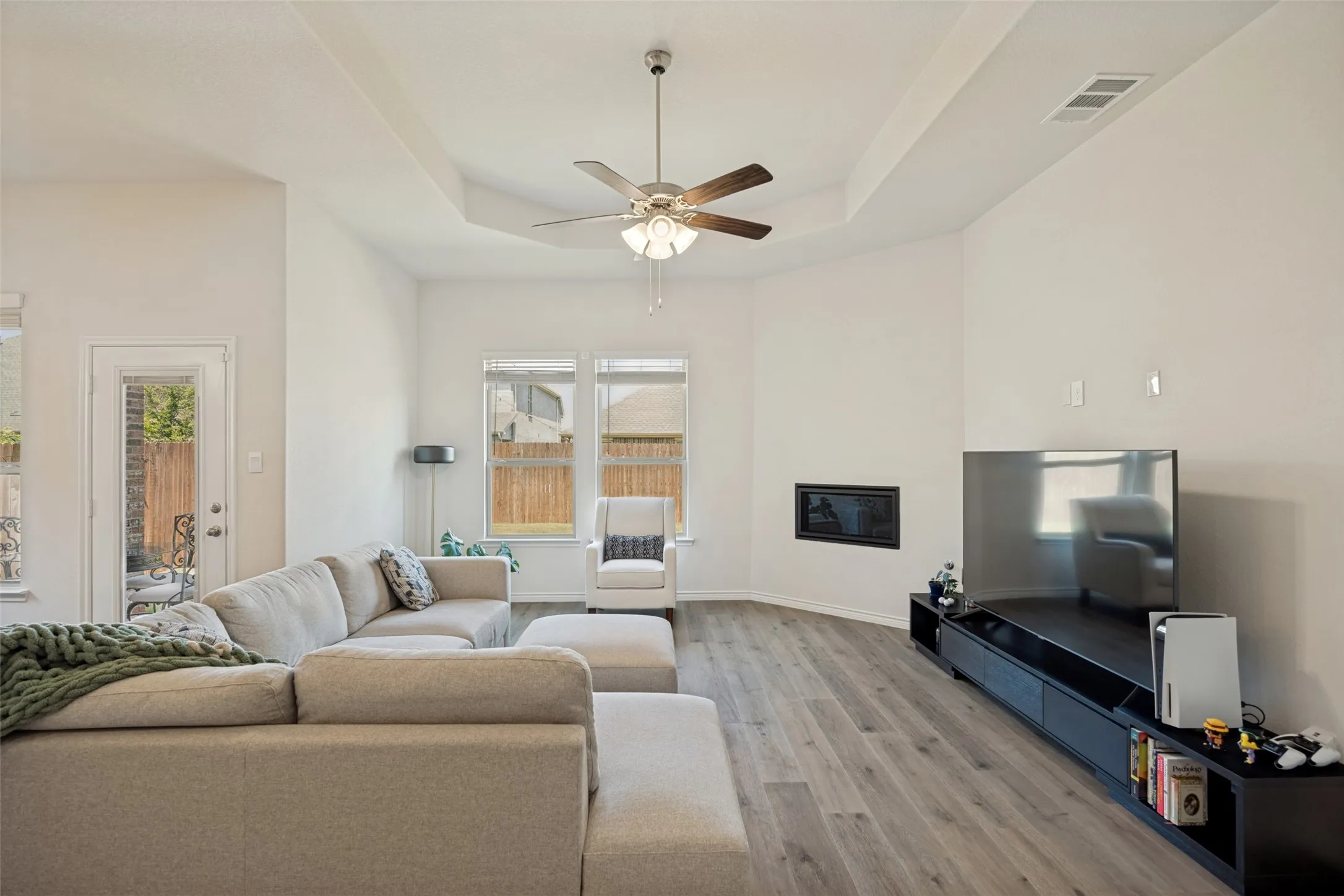 Tray ceiling with a ceiling fan, wood-finish flooring, multiple windows, and a built-in fireplace