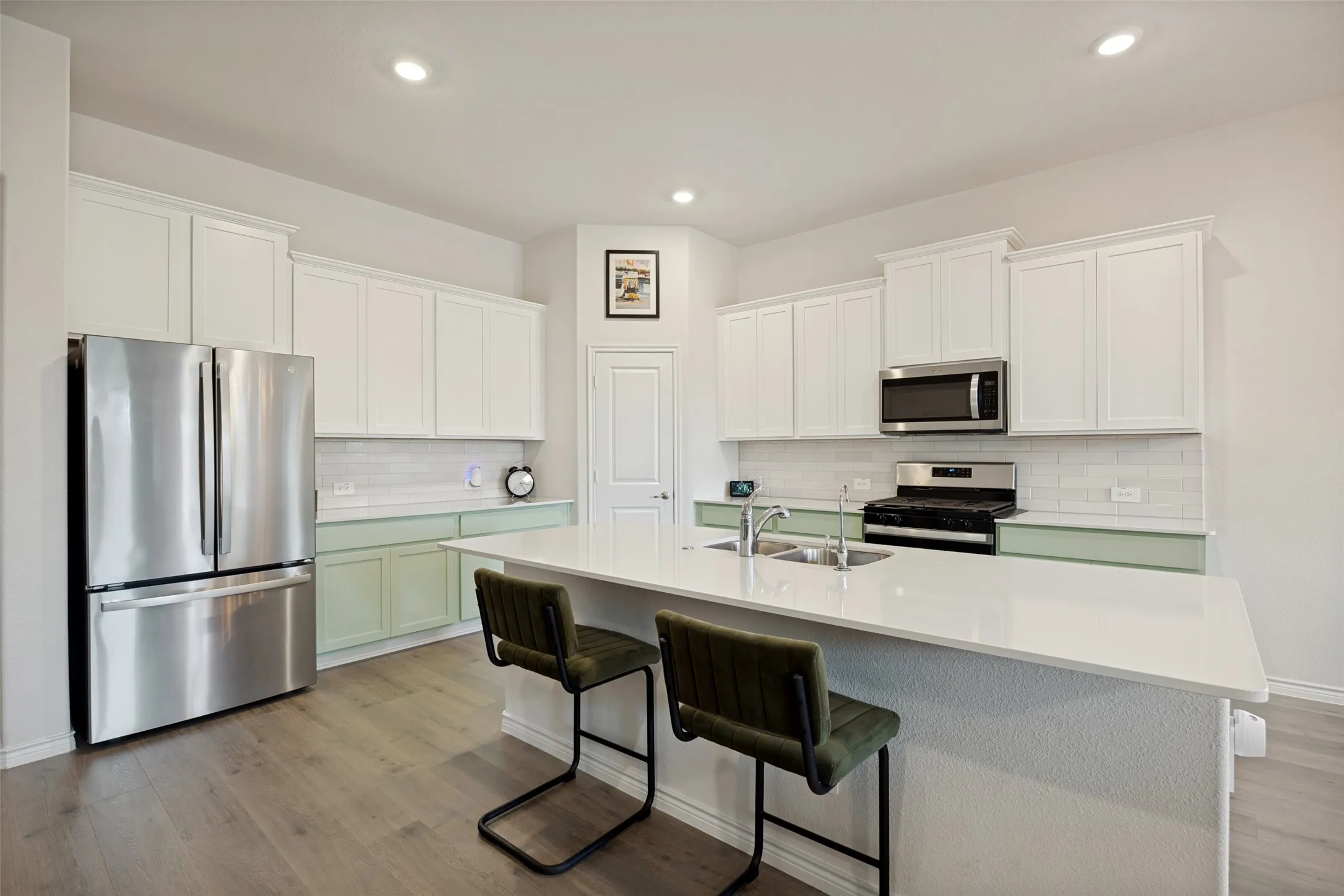 White shaker-style cabinetry, stainless steel appliances, light wood-finish flooring, white countertop island, and subway tile backsplash