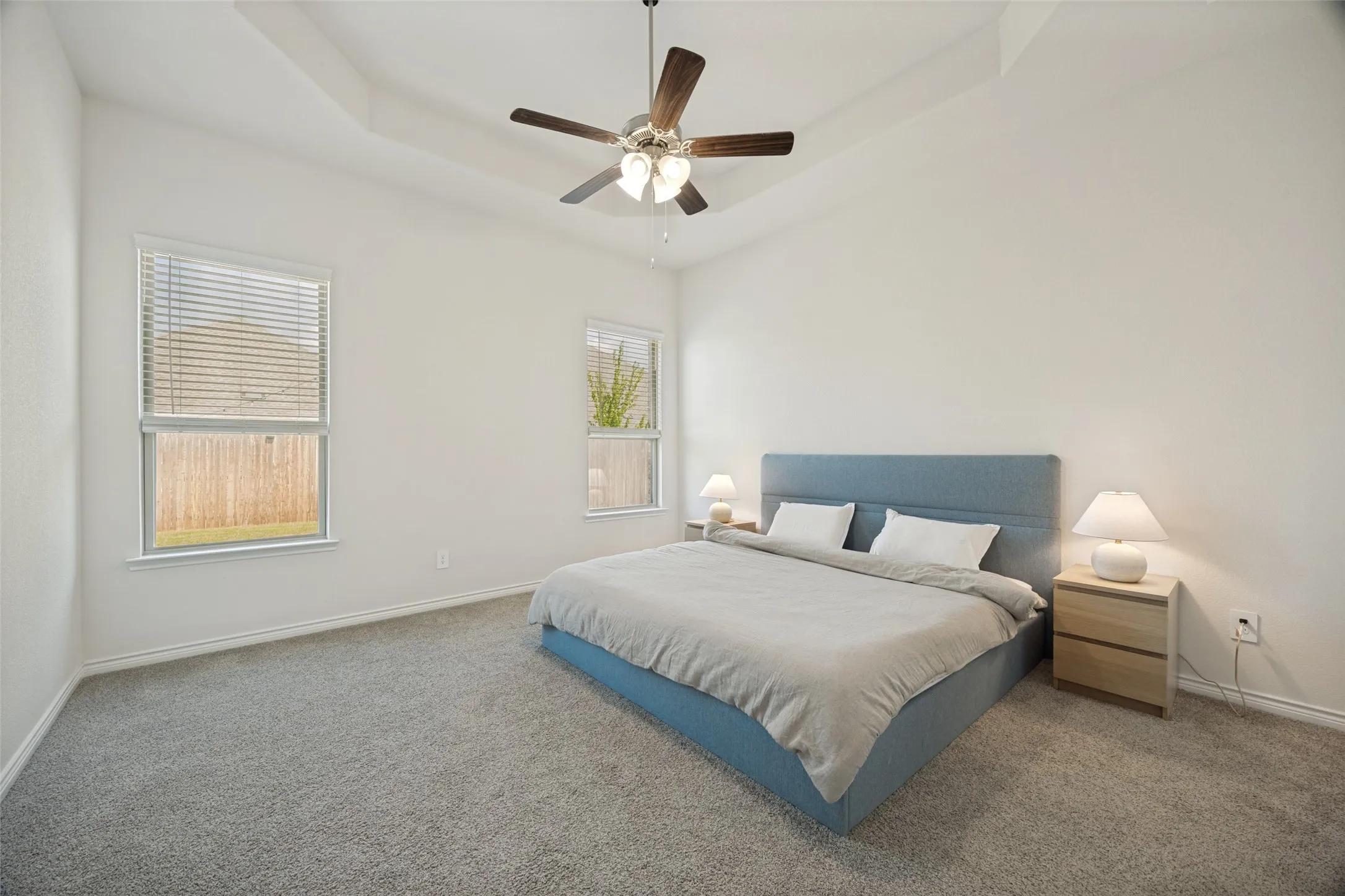 Tray ceiling with a ceiling fan, two windows, and gray carpeting
