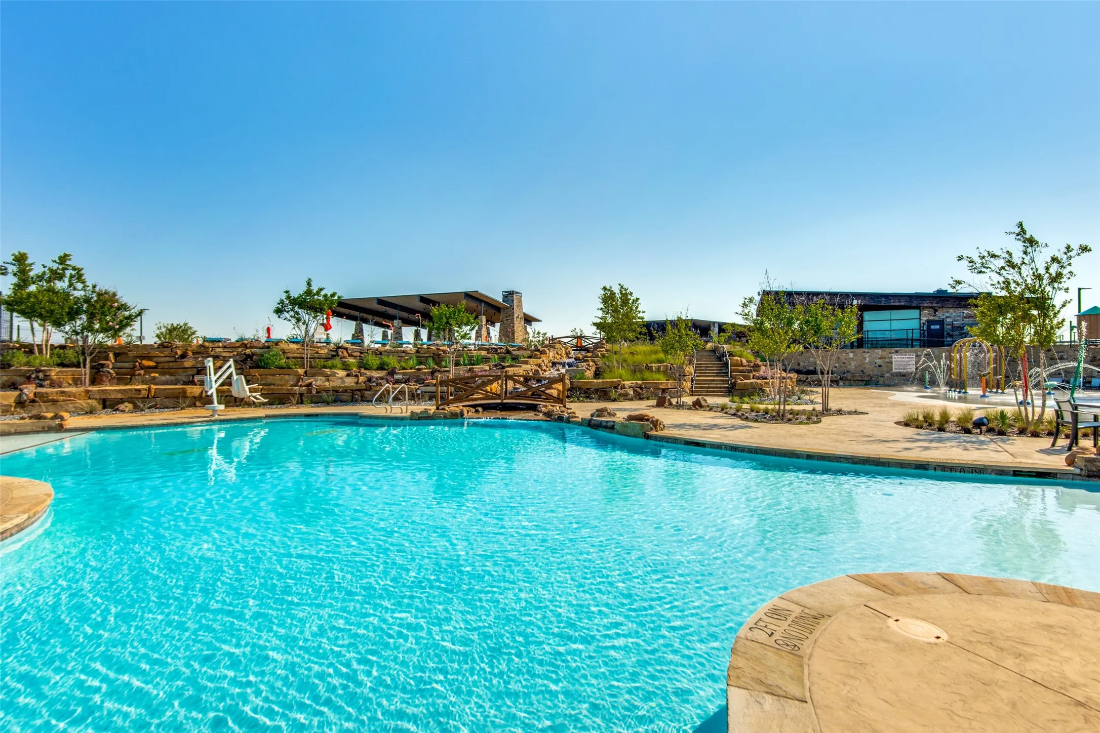 Expansive outdoor swimming pool with stone decking, a shaded pergola, and a water play area