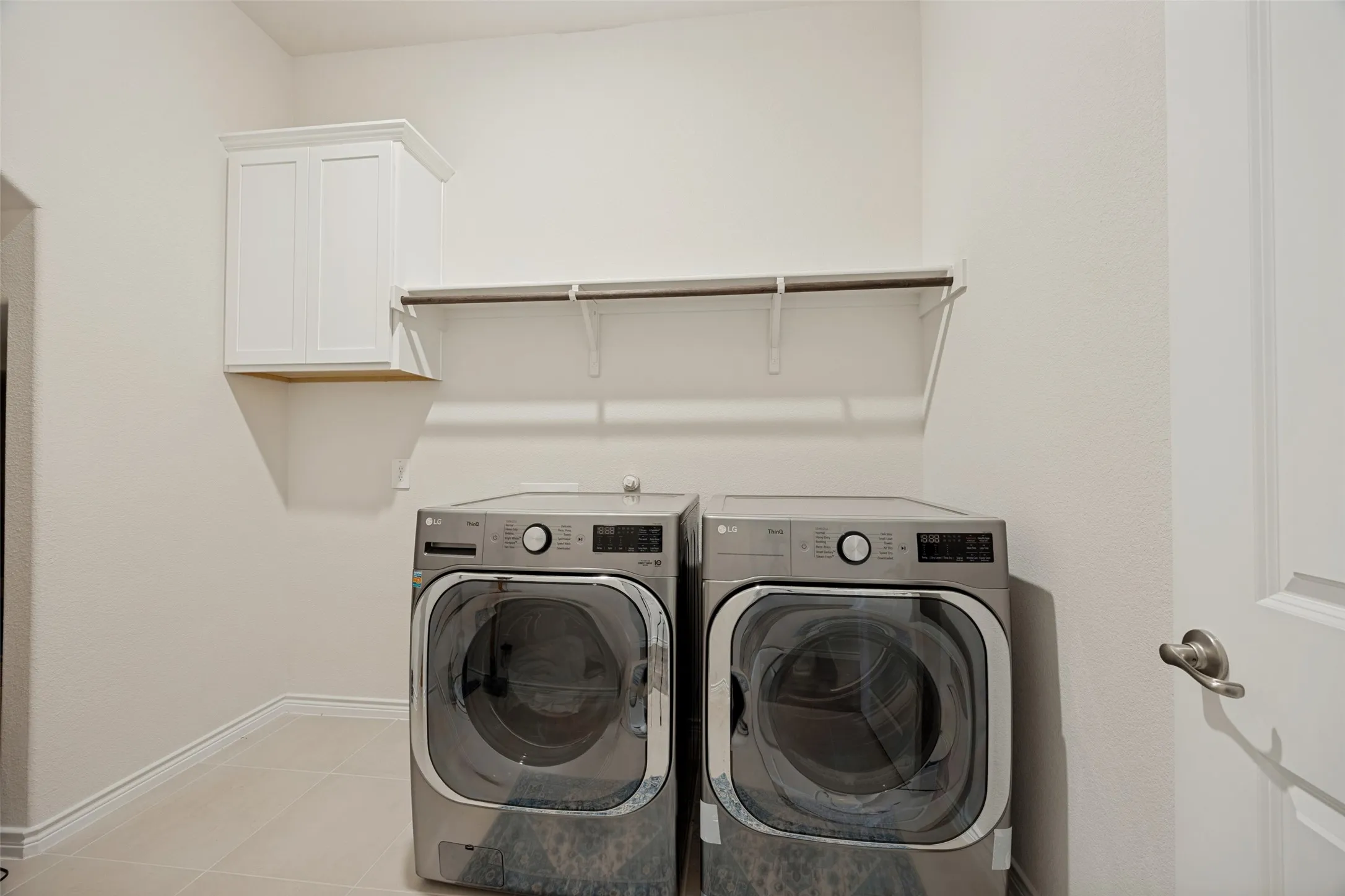 White cabinetry, light-toned tile flooring, and a mounted shelf for organization