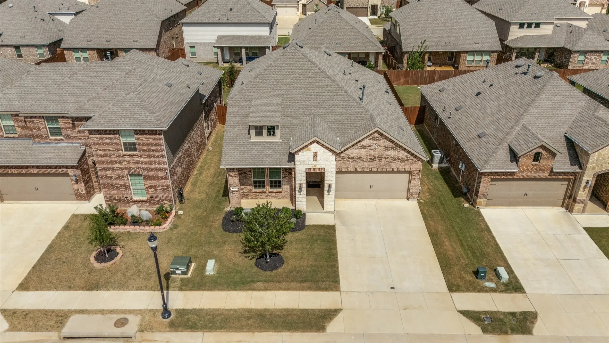 Brick exterior with stone accents, attached two-car garage, concrete driveway, and front yard landscaping