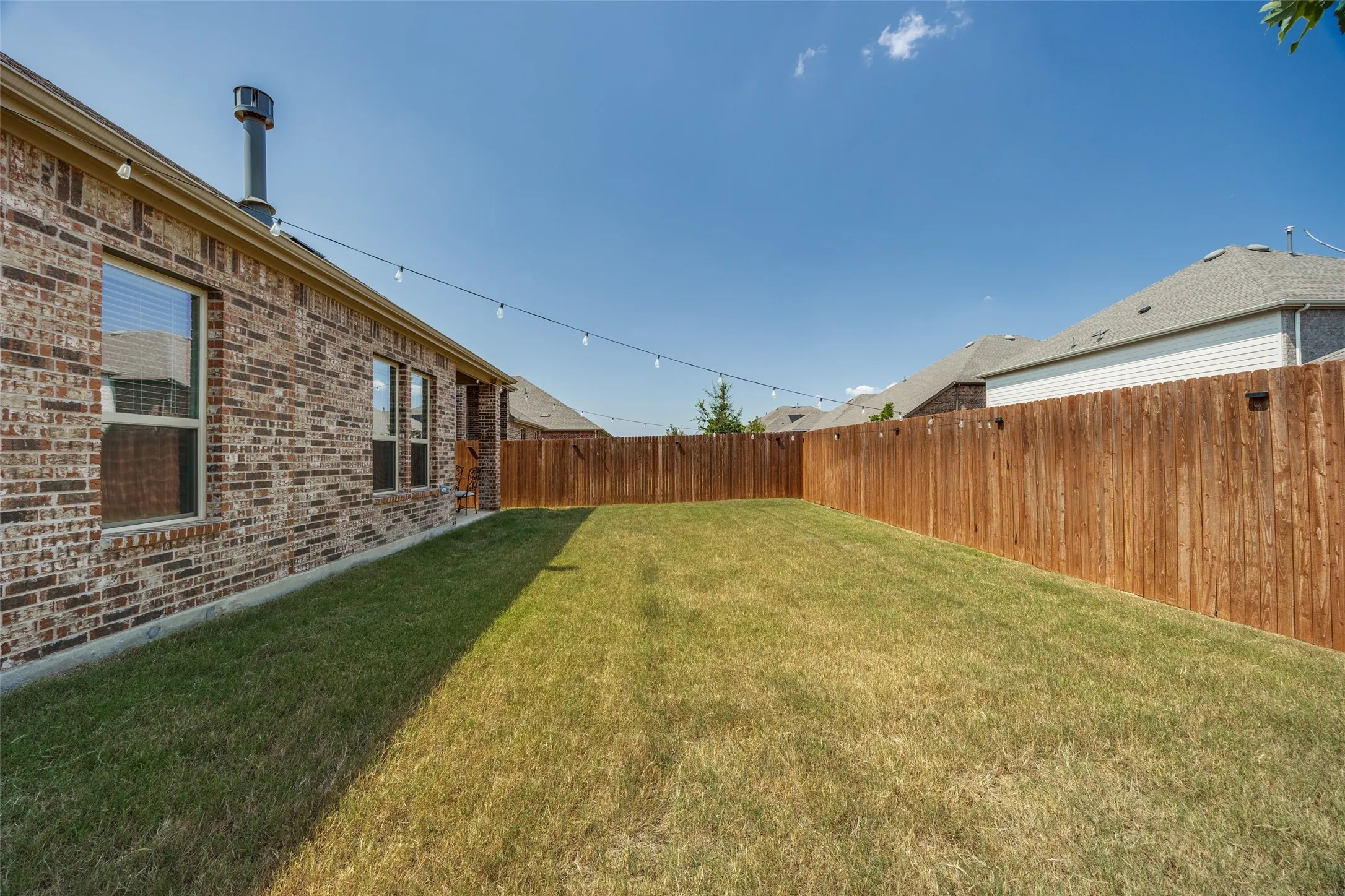 Expansive grassy backyard featuring a full privacy fence and a brick exterior
