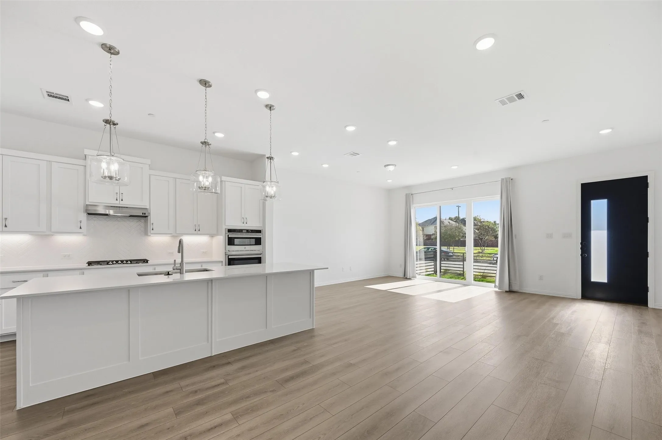 Open-concept living space with wood-finish flooring, white cabinetry, a kitchen island, recessed lighting, and a sliding glass door