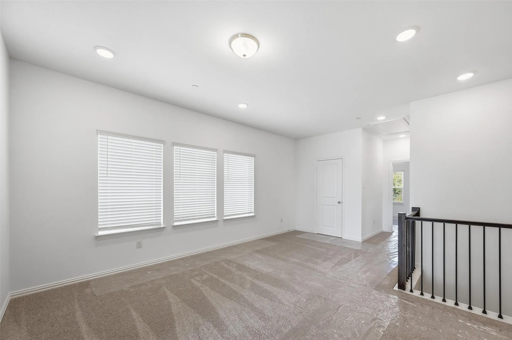 Carpeted living space with multiple windows, recessed lighting, and a white paneled door