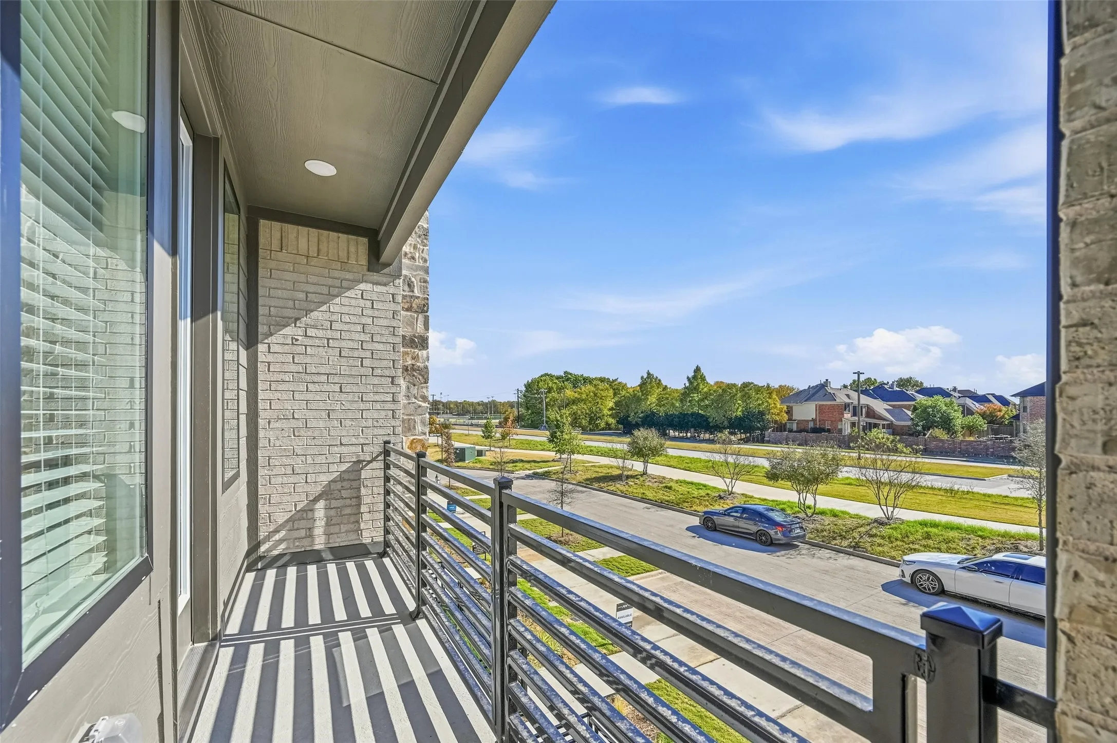 Balcony with a horizontal metal railing, recessed lighting, and a brick exterior wall