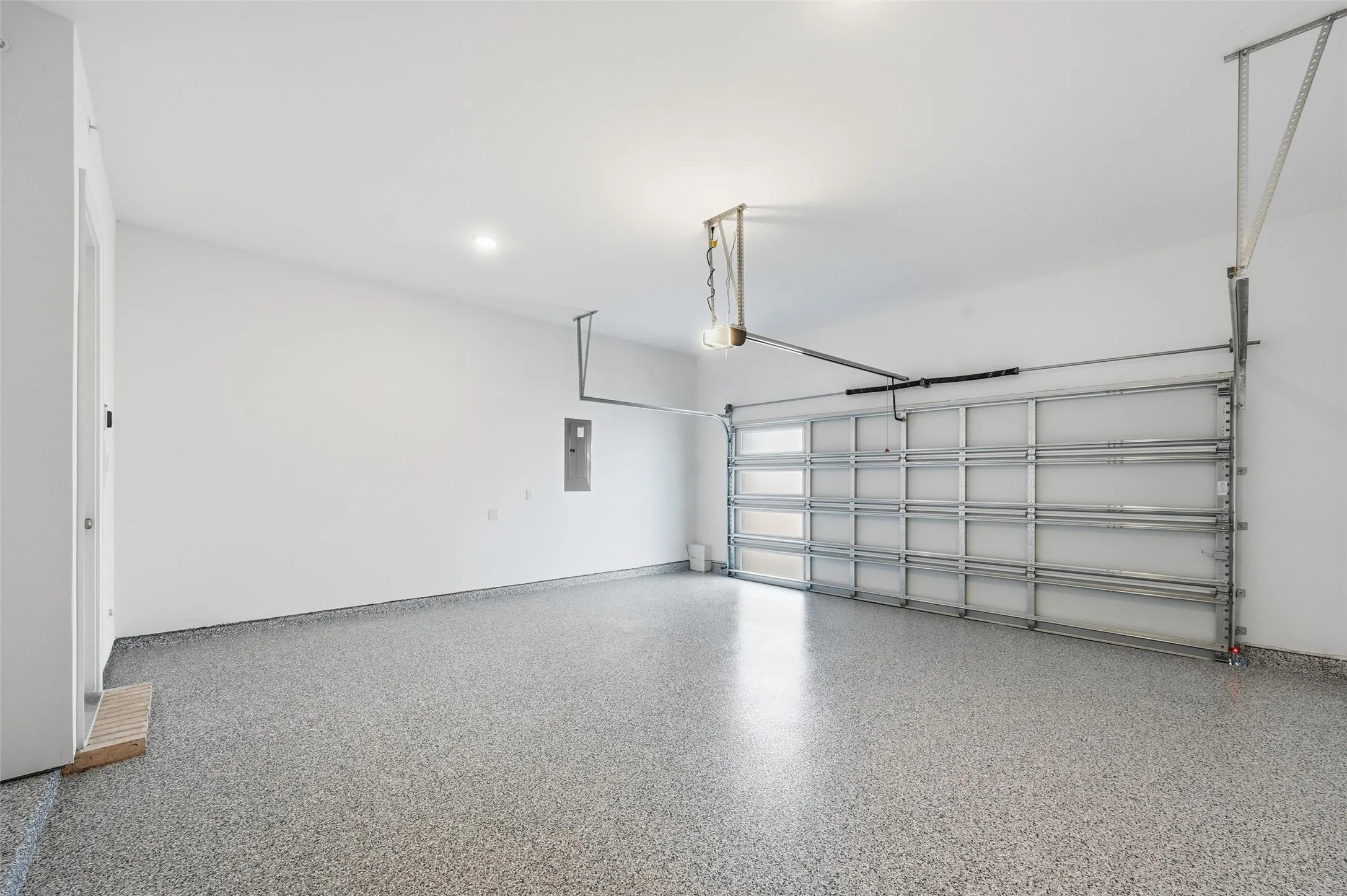 Expansive garage featuring a speckled epoxy floor, overhead lighting, and an automatic garage door opener