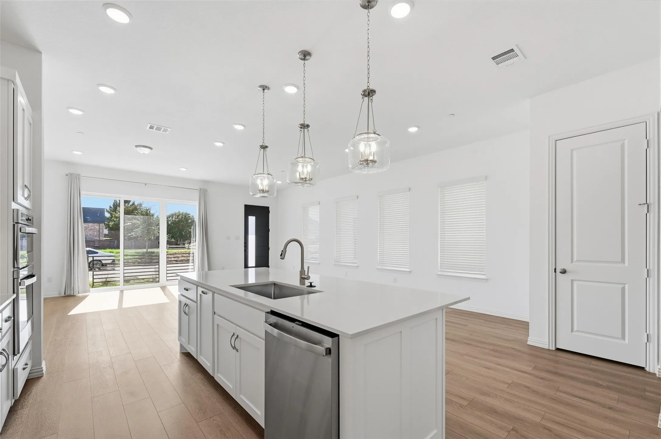 Open-concept living space featuring a kitchen island with sink, stainless steel appliances, wood-finish flooring, recessed lighting, and a sliding glass door