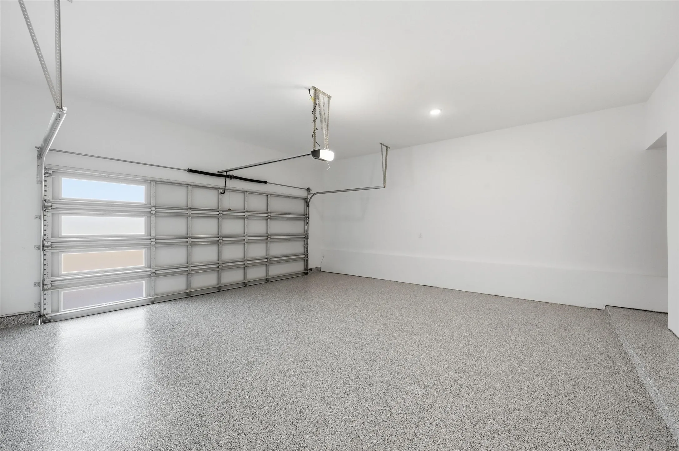 Garage space featuring an epoxy-coated floor, automatic garage door opener, and recessed lighting