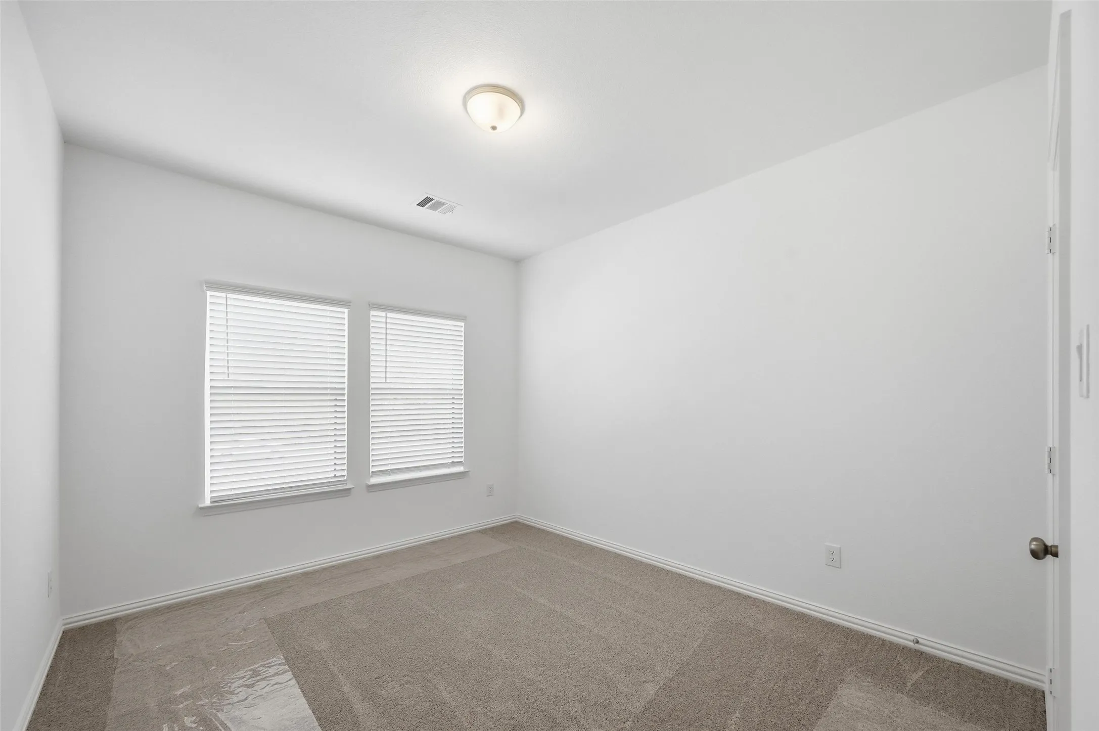 Neutral wall paint, carpet flooring, windows with blinds, and a flush mount ceiling light