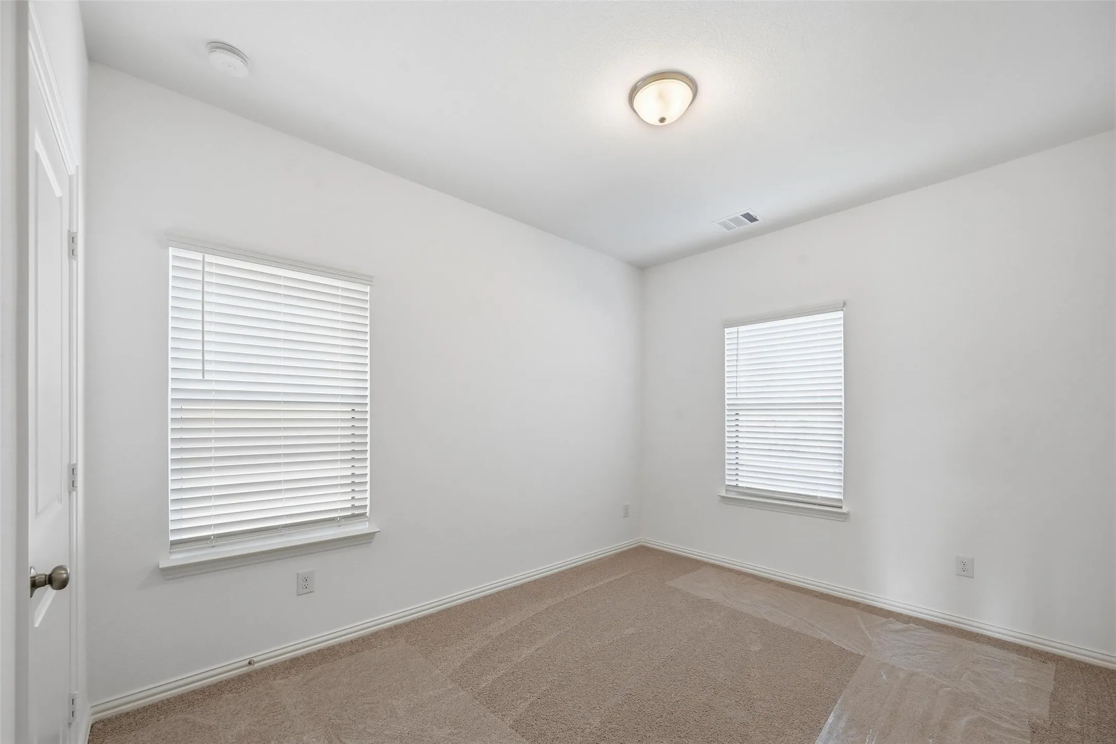 Wall-to-wall carpeting, two windows with blinds, a flush mount ceiling light, and a white interior door