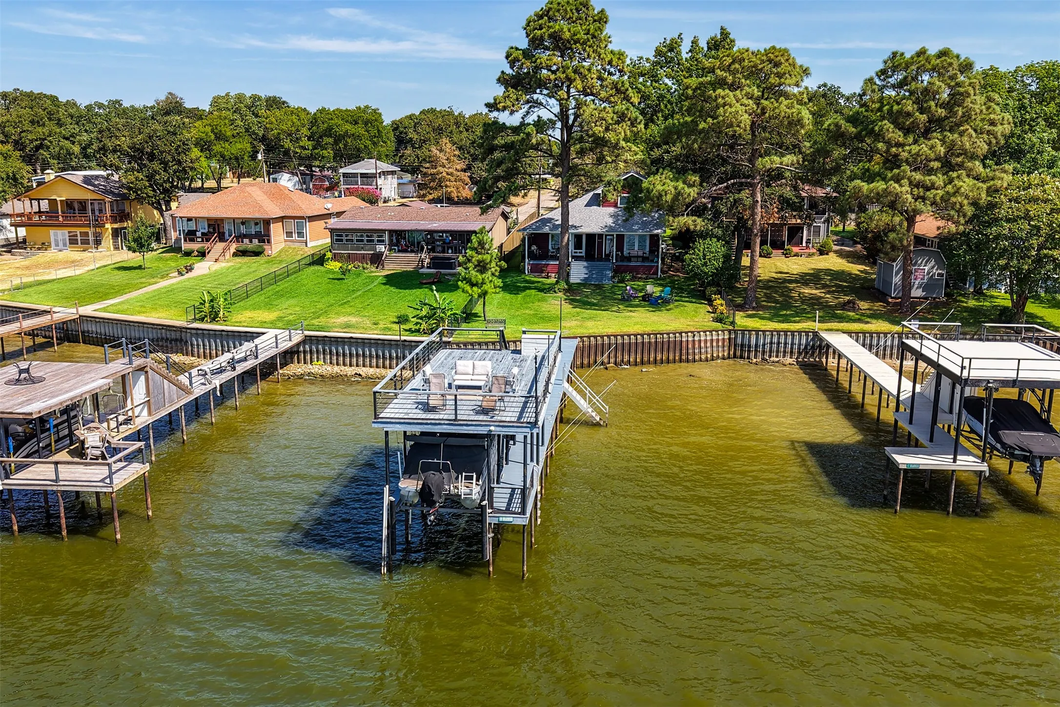 Waterfront property featuring a private boat dock with an upper-level deck, a second boat dock with a covered slip, and a manicured grassy lawn