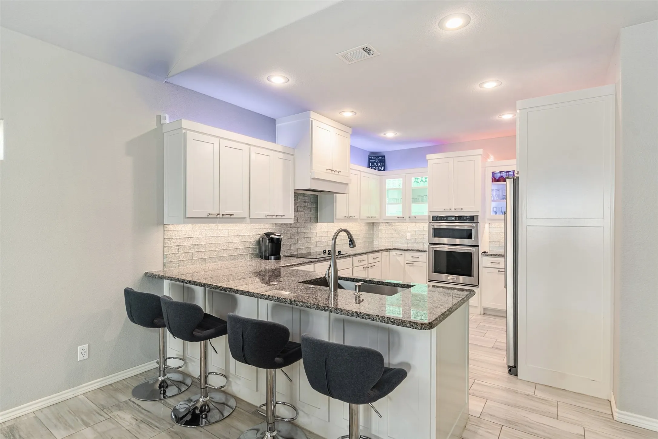 Modern kitchen featuring white shaker-style cabinetry, stainless steel appliances, subway tile backsplash, and a waterfall-edge island with dark granite countertops