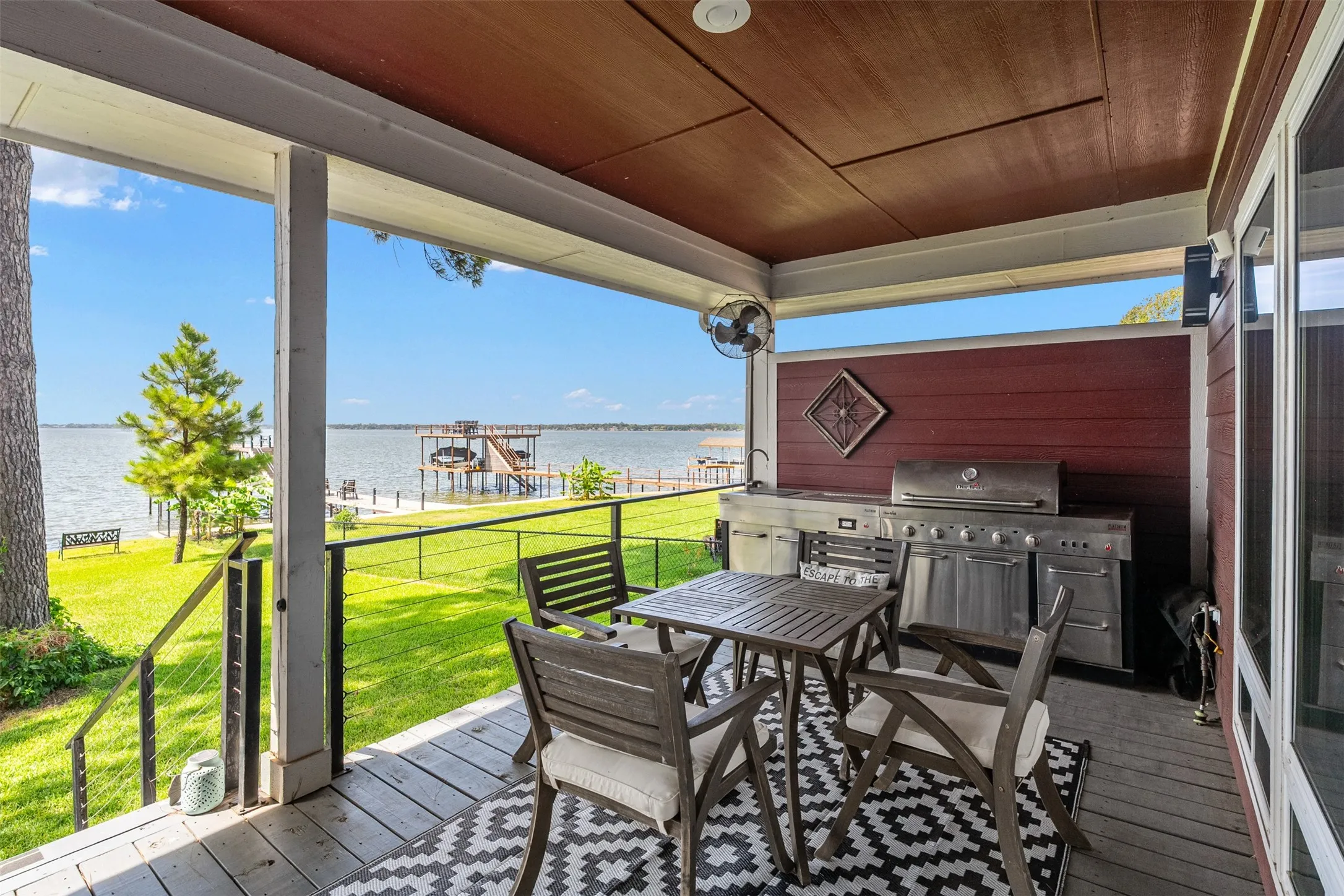 Covered porch with wood flooring, featuring an outdoor kitchen with a built-in grill, and a railing system