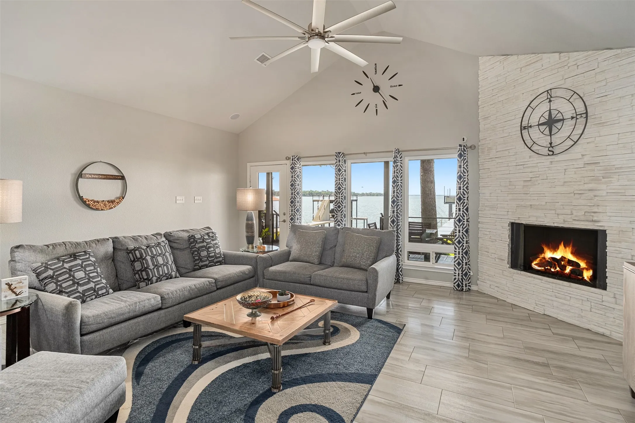 Vaulted ceiling with an installed ceiling fan, floor-to-ceiling windows, modern fireplace with a stacked stone surround, and Tile flooring