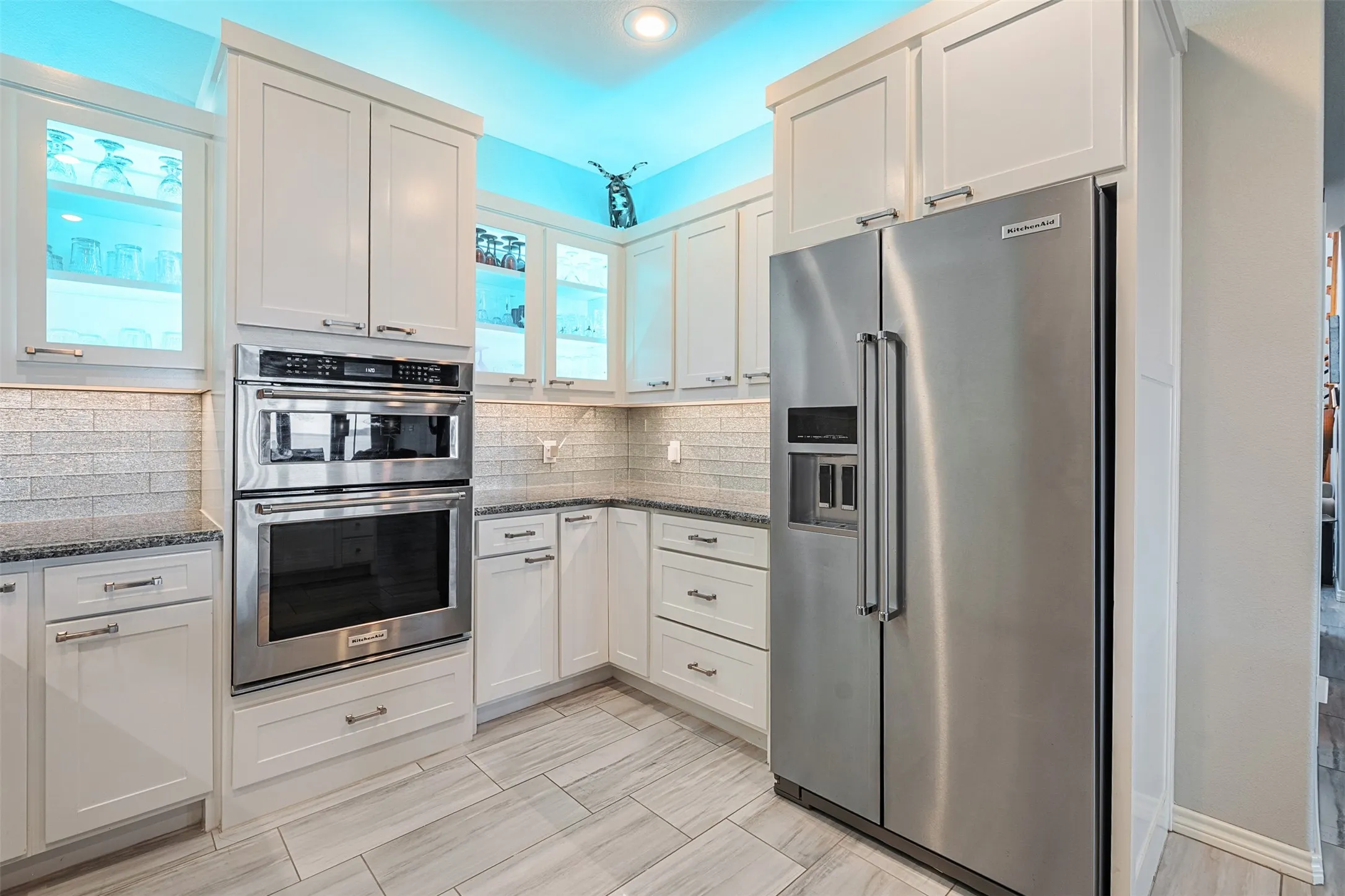 White cabinetry, stainless steel microwave and oven, stainless steel refrigerator, granite countertops, and light-toned tile flooring