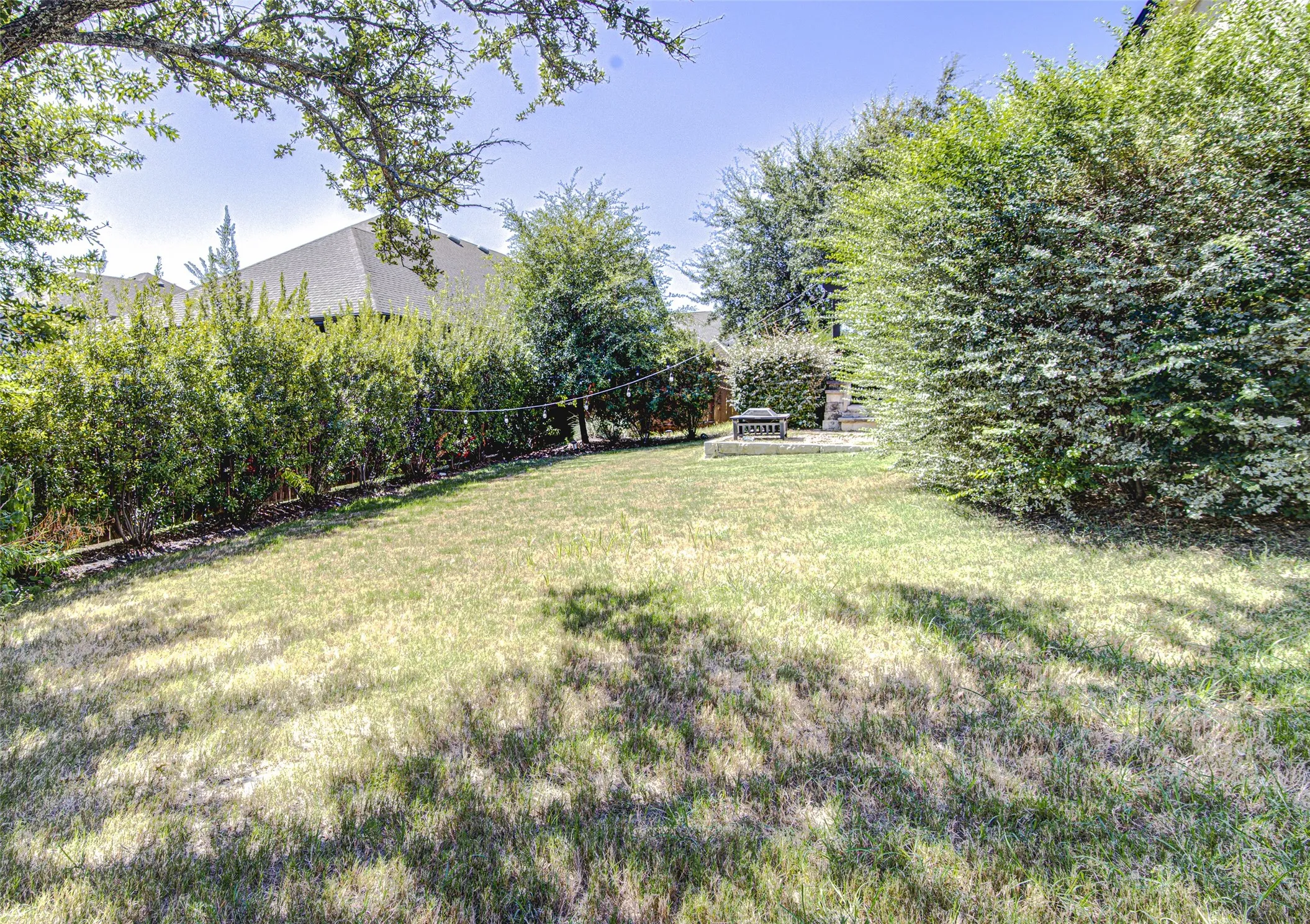 Expansive backyard with a manicured lawn, established privacy hedges, and a dedicated patio area featuring a fire pit