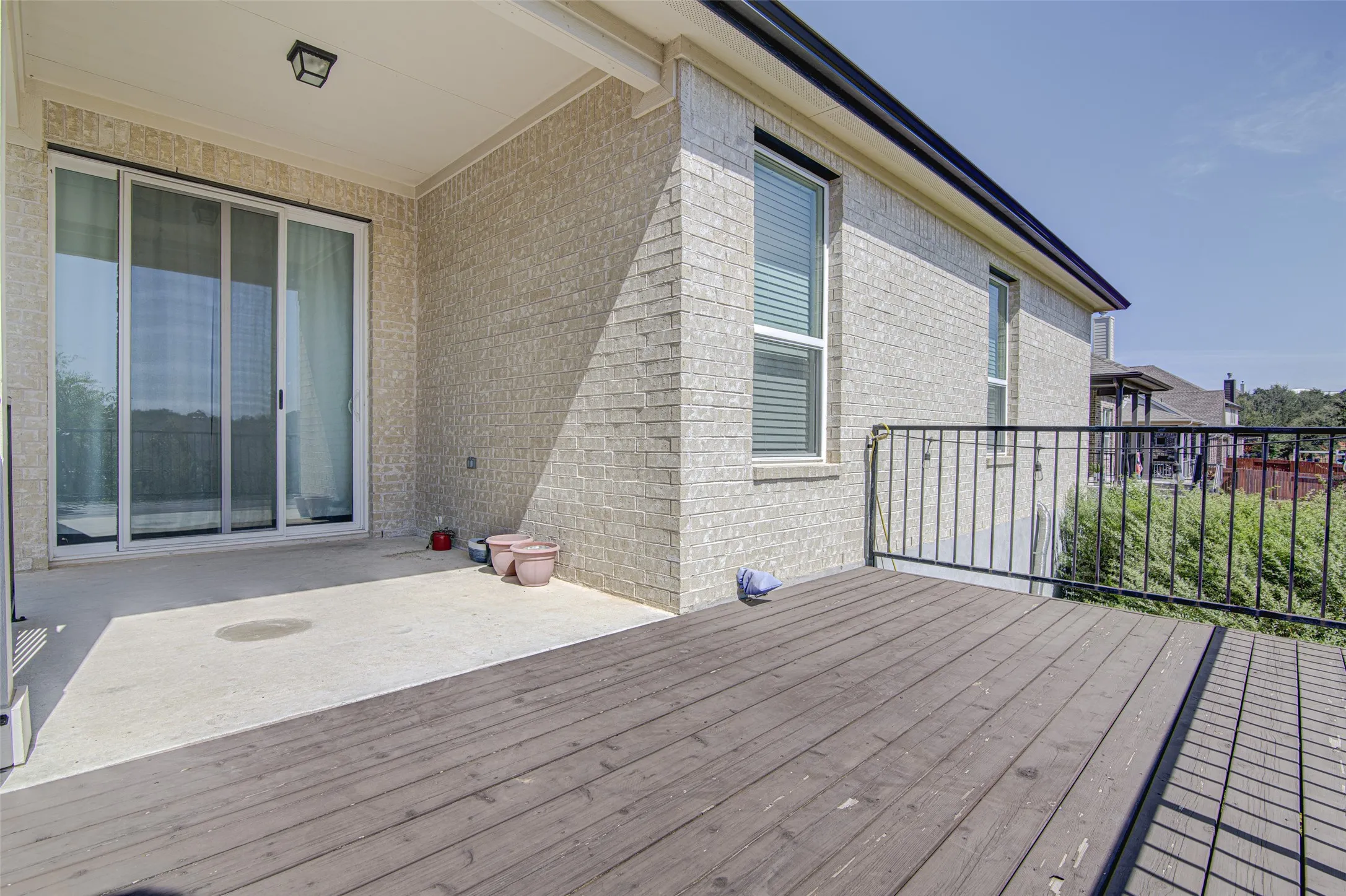 Expansive outdoor living area featuring a covered concrete patio, a wood-finish deck, and black metal railings