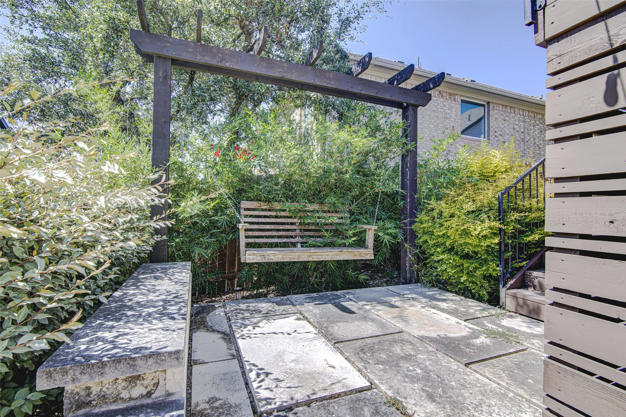 Stone slab patio with a built-in stone bench, wood pergola, and wood porch swing