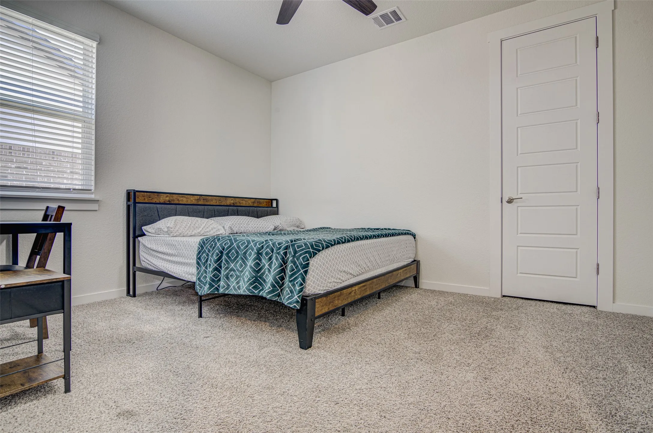 Neutral wall color, carpeted flooring, window with blinds, paneled interior door with lever hardware, and ceiling fan