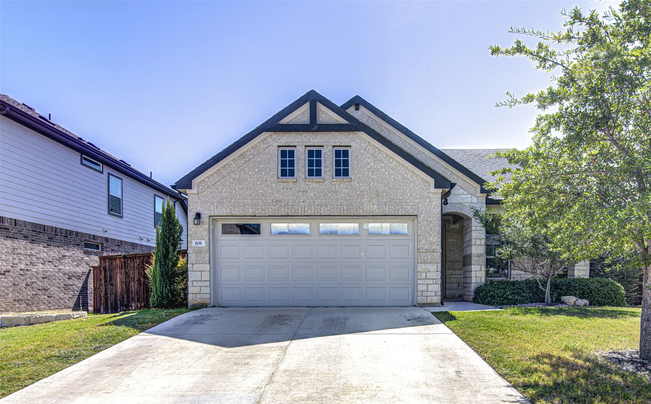Stone and siding exterior with a two-car garage, concrete driveway, and established landscaping