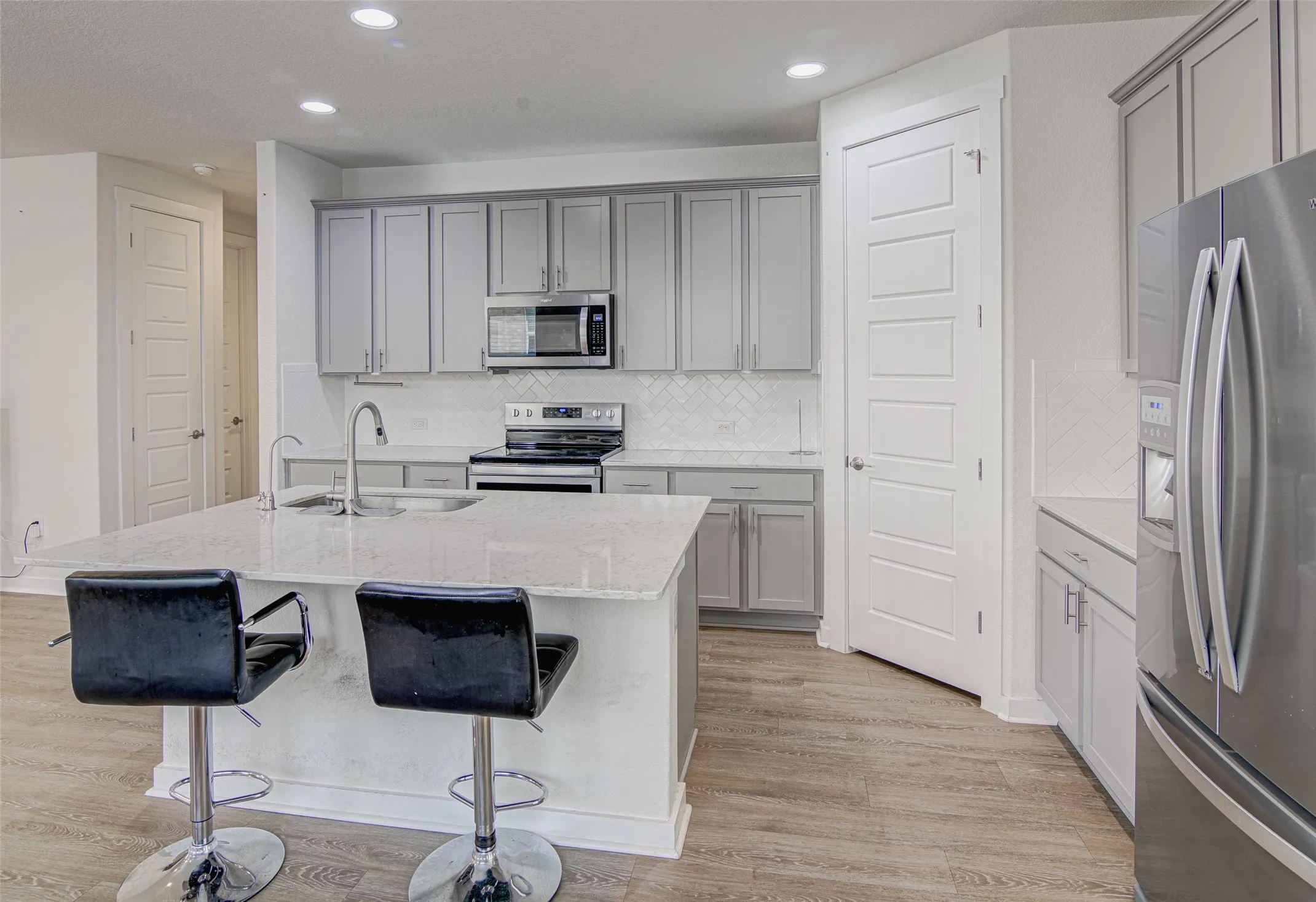 Kitchen featuring light gray cabinetry, stainless steel appliances, a center island with sink, white countertops, and wood-finish flooring