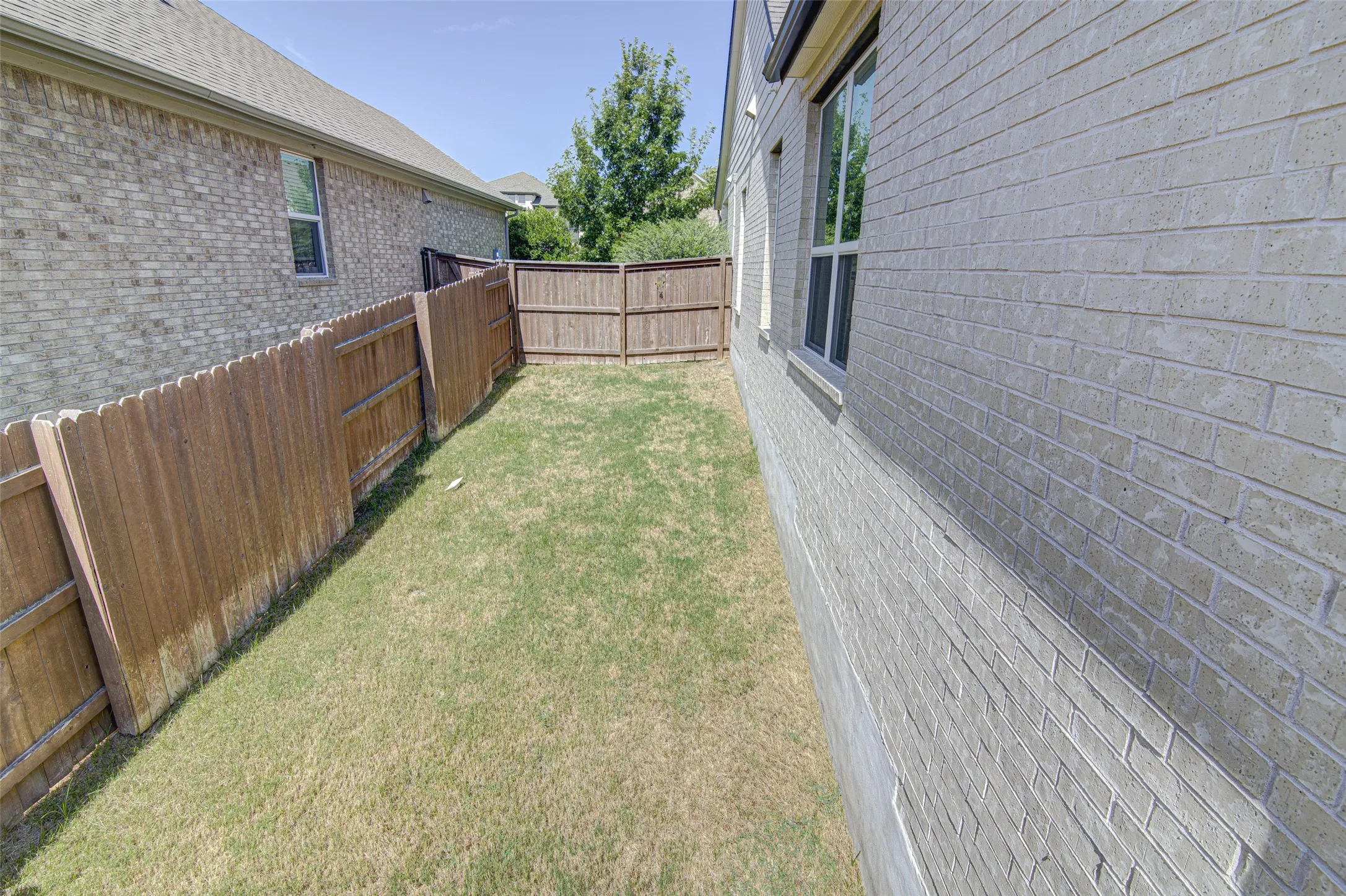 Enclosed backyard featuring a wooden privacy fence, a brick exterior, and a window with white trim