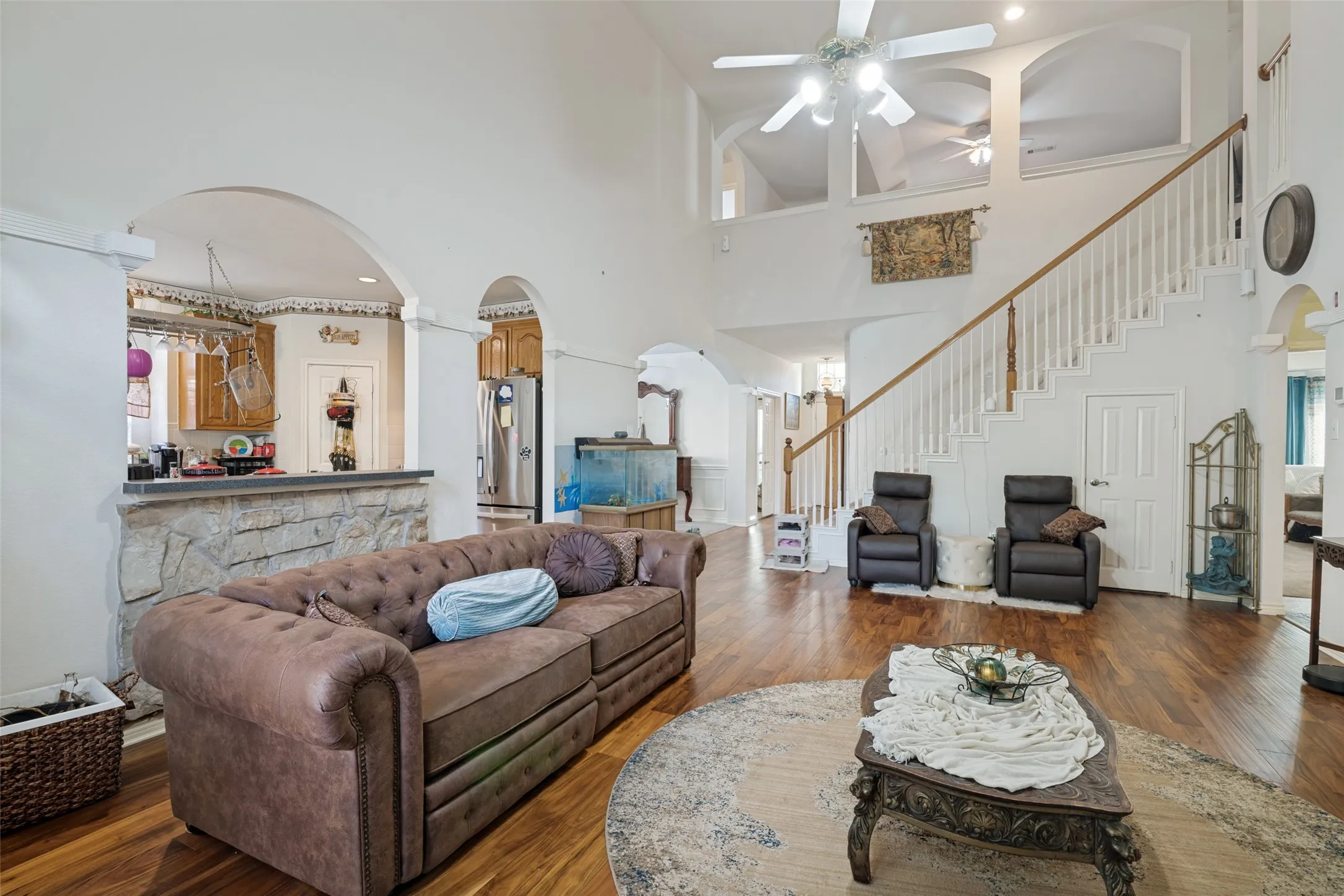 Two-story living space featuring wood-finish flooring, a grand staircase with white balusters and wood handrail, and high ceilings with ceiling fans