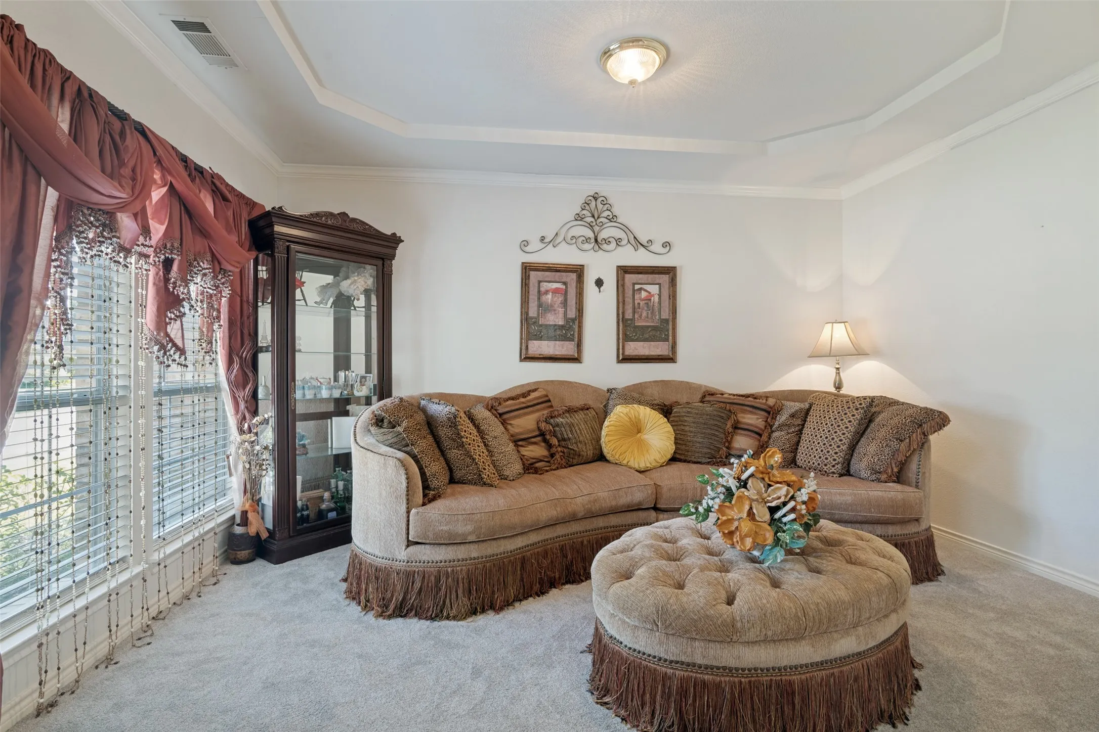 Tray ceiling with crown molding, carpeted flooring, large window with blinds, recessed ceiling light fixture, and built-in display cabinet