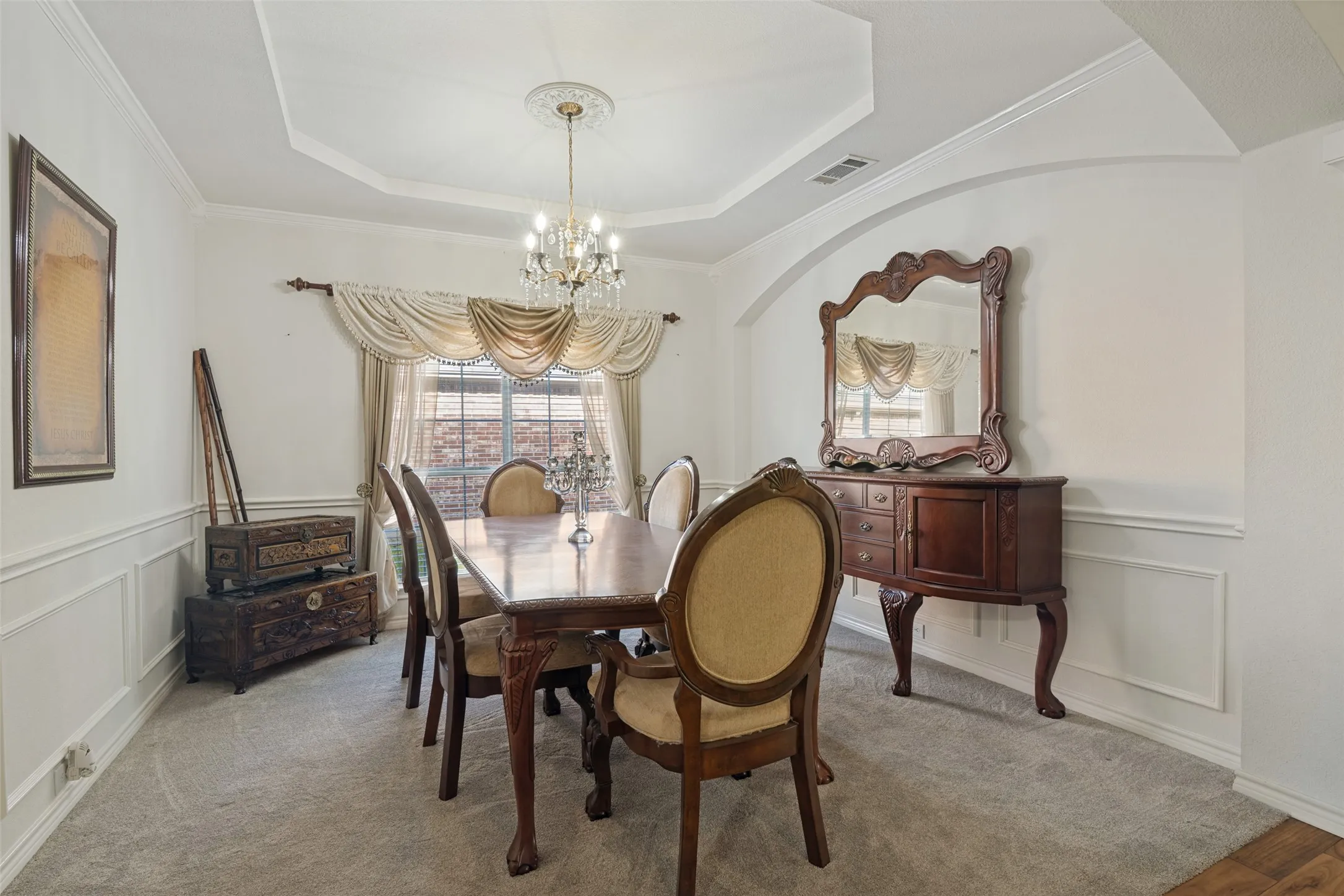 Tray ceiling with crown molding, chandelier lighting, arched doorway, and wainscoting details