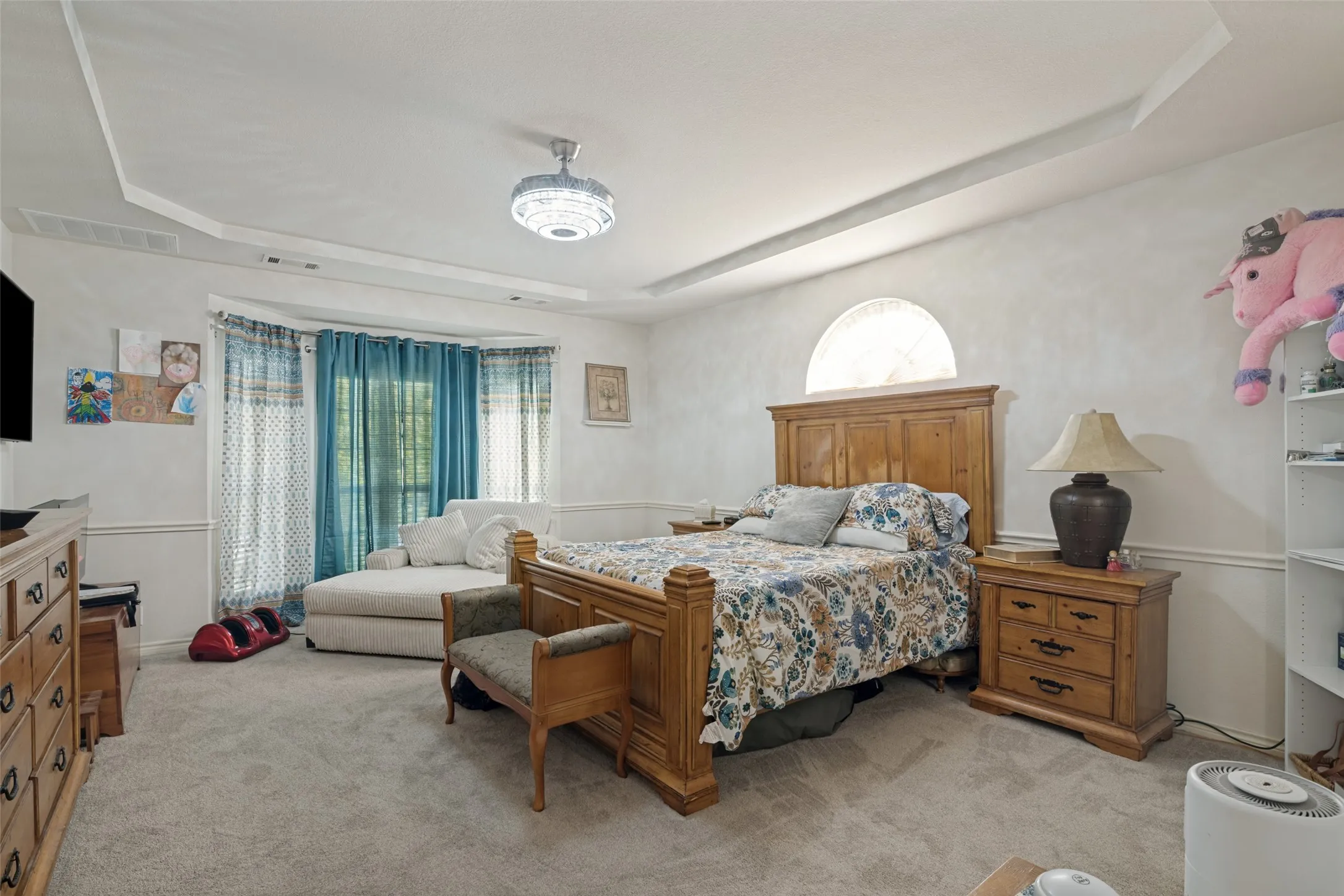 Tray ceiling with a decorative lighting fixture, arched window, and bay window with layered window treatments